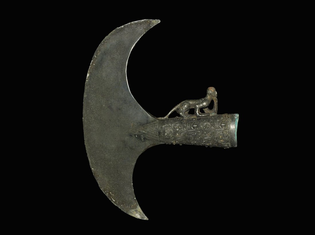 Chinese Style Bronze Axe with Walking Monkey: An undated archaistic axe head with elliptical-section socket and peltoid blade; the socket ornamented with raised geometric scrolled designs; above, a model monkey cast in the round, with chin restin