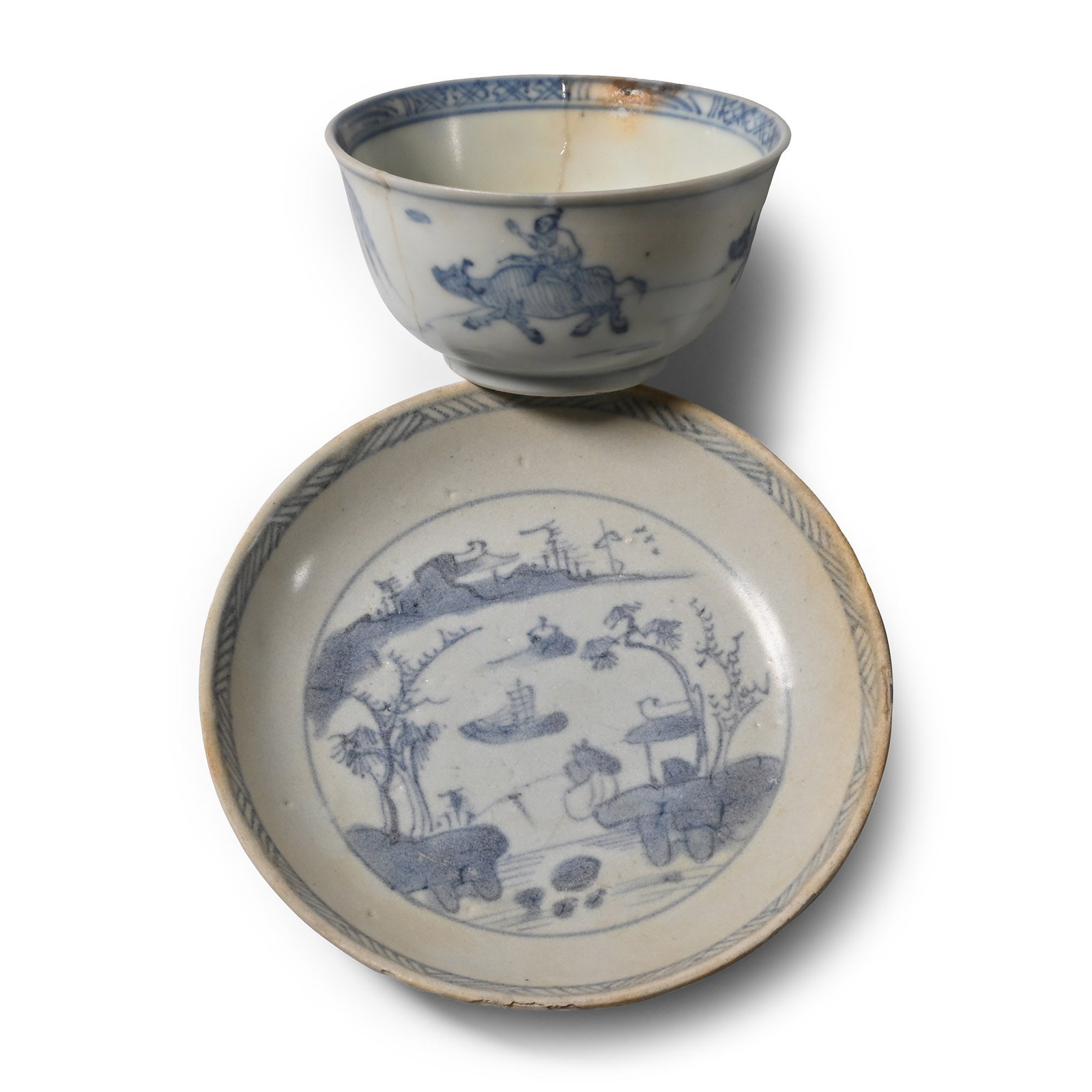 Ca Mau Cargo Shipwreck Glazed Blue and White Tea Bowl and Saucer: Early 18th century A.D. Comprising a shallow bowl with a lakeside scene showing a fisherman on the foreground, two floating junks on the lake and buildings in the distance; the bowl with a painted sce