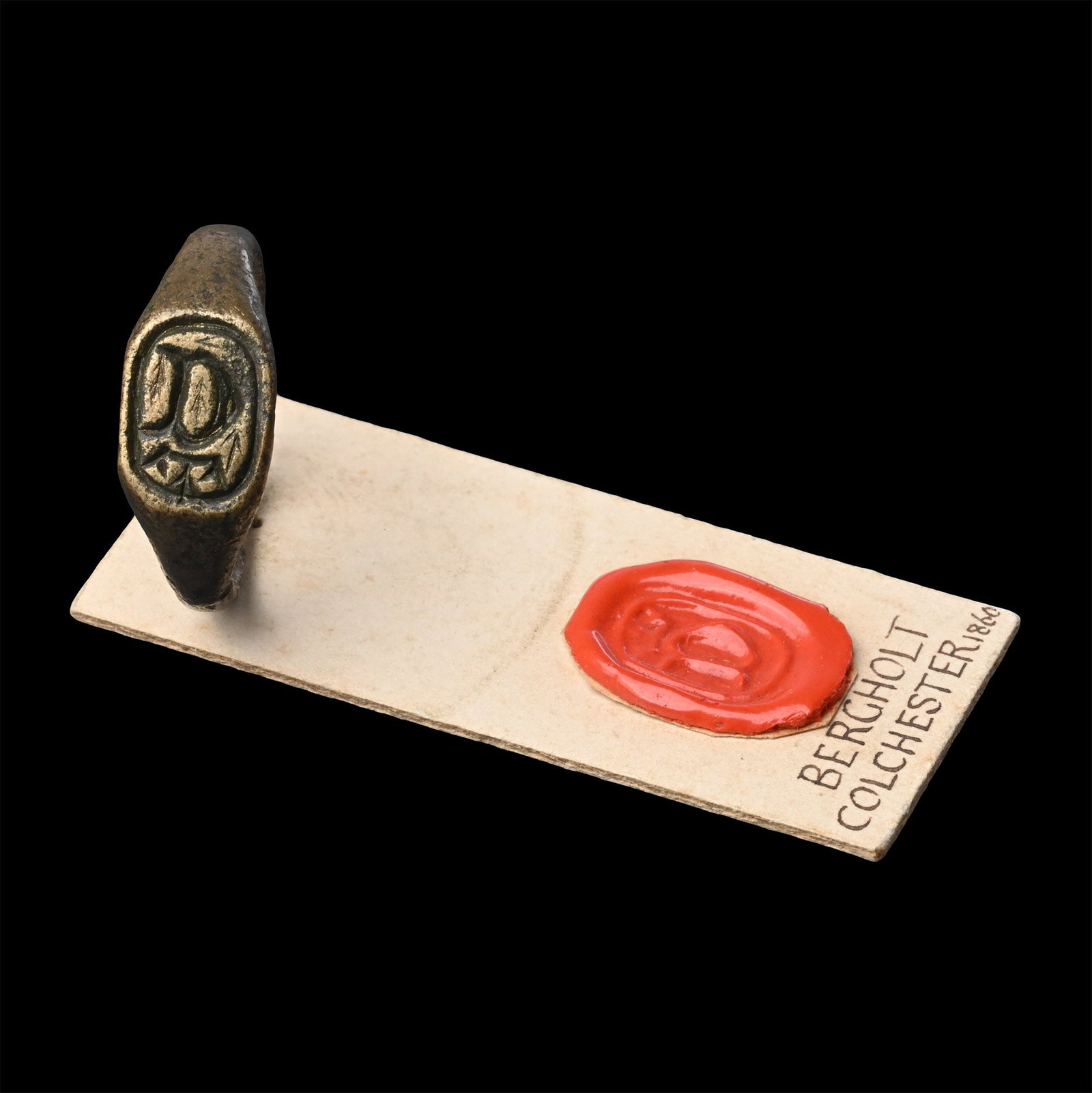 Large Medieval Bronze 'Bergholt, Colchester' Signet Ring with Crowned D: 15th-16th century A.D. D-section hoop and ellipsoid bezel with 'D' beneath a crown; attached to a collector's card with sample seal impression and legend 'Bergholt Colchester 1860'. 8.69 grams total,