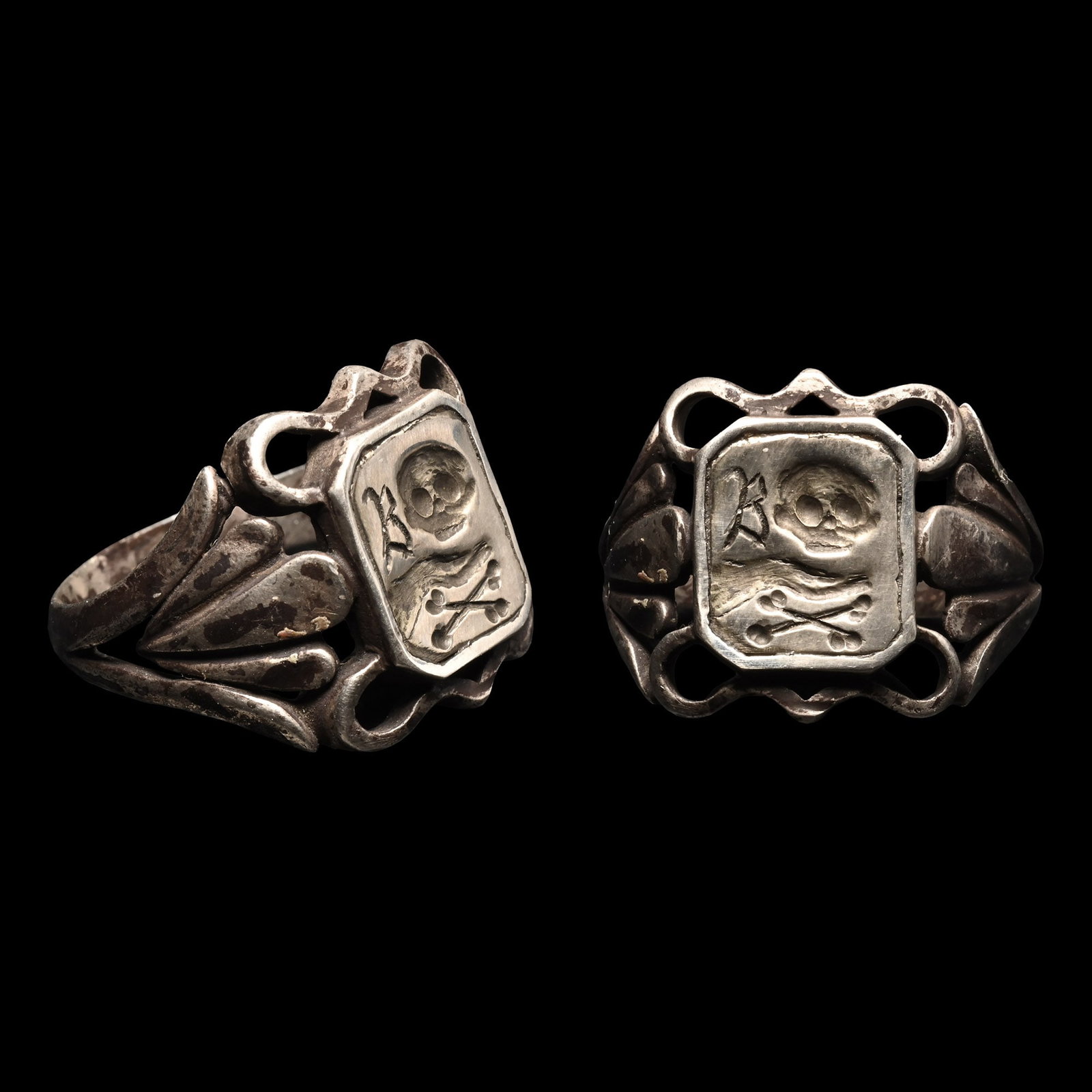 Post Medieval Silver Memento Mori Ring with Skull and Crossed Bones: 18th-19th century A.D. Openwork fronds to the shoulders, rectangular plaque with raised border, incuse skull motif over two long bones crossed, script capital 'B'. 7.9 grams, 24.6 mm overall, 21.29 mm