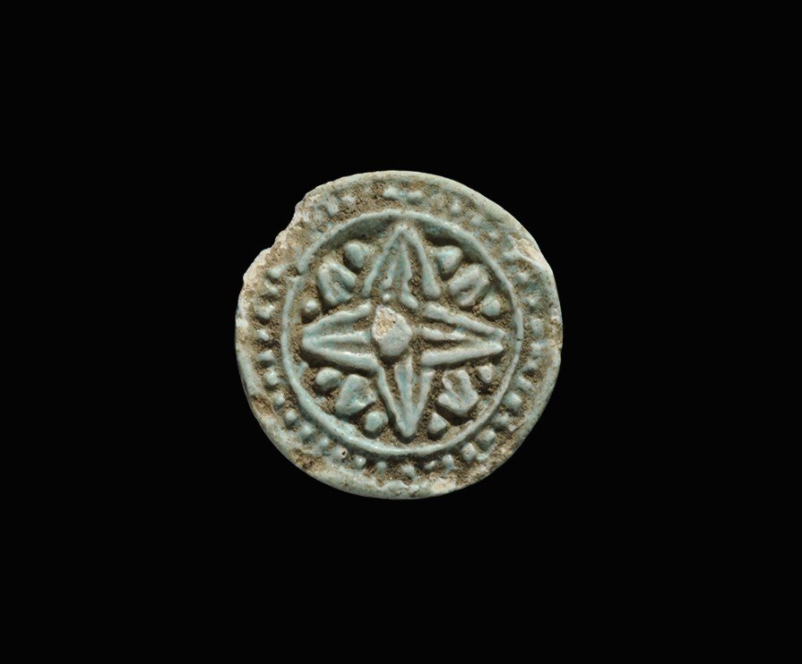 Egyptian Glazed Composition Rosette Amulet: Late Period, 664-332 BC. A discoid amulet with intaglio rosette to the underside surrounded by a band of pellets; pierced to the reverse. 3.24 grams, 26 mm (1"). From a collection of Egyptian artefact