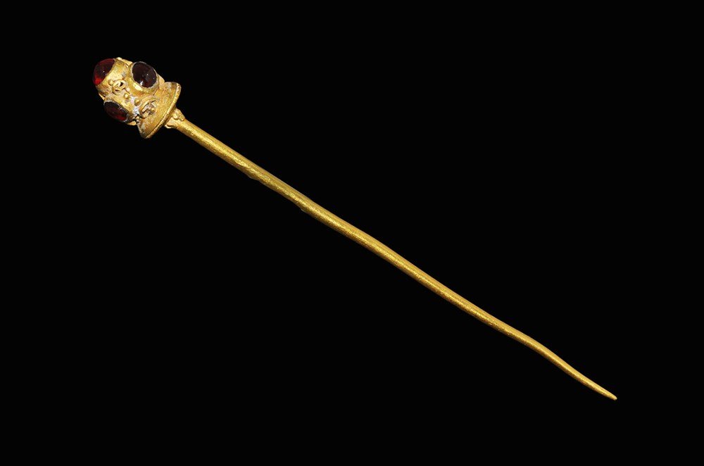 Byzantine Gold Pin with Cabochon Garnets: 5th-8th century AD. A gold dress pin with tapering shaft, biconical terminal with granules below, filigree fillet to the edge; the upper face supporting three elliptical cabochon garnets in cells with