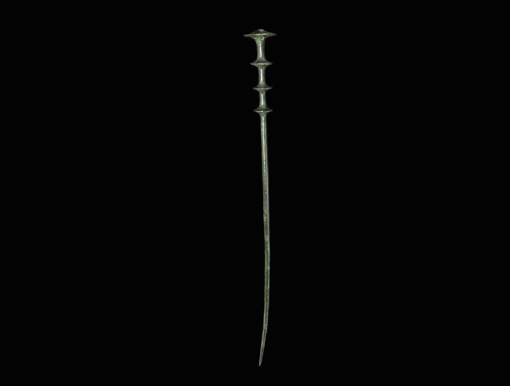 Bronze Age Large Cloak Pin: 1500-900 BC. A long central European bronze cloak pin, the head with four graduated projecting collars, the shaft ornamented with bands of incised rings and chevrons. 68 grams, 30 cm (12"). Property o