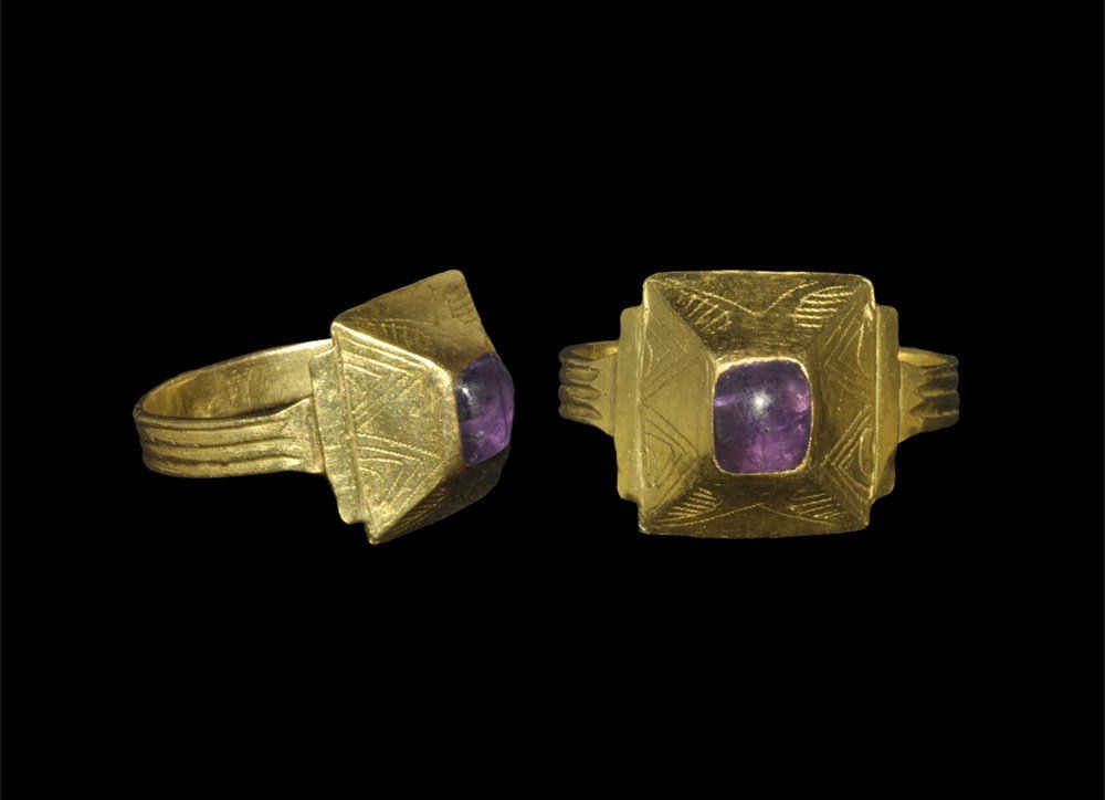 Medieval Gold Bishop's Ring with Amethyst Cabochon: 12th century AD. A large flat-section hoop with ribbed exterior supporting a pyramidal bezel with incised geometric motifs, inset cabochon amethyst to the centre. 8.73 grams, 29 mm overall, 20.67 mm i