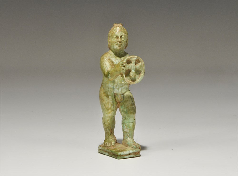 Byzantine Style Bone Putto Figurine: An undated archaistic carve figurine of an advancing nude putto on a rectangular base, holding up a discoid plaque with central cross motif to the recess. 22 grams, 75 mm (3"). Property of a London Ge