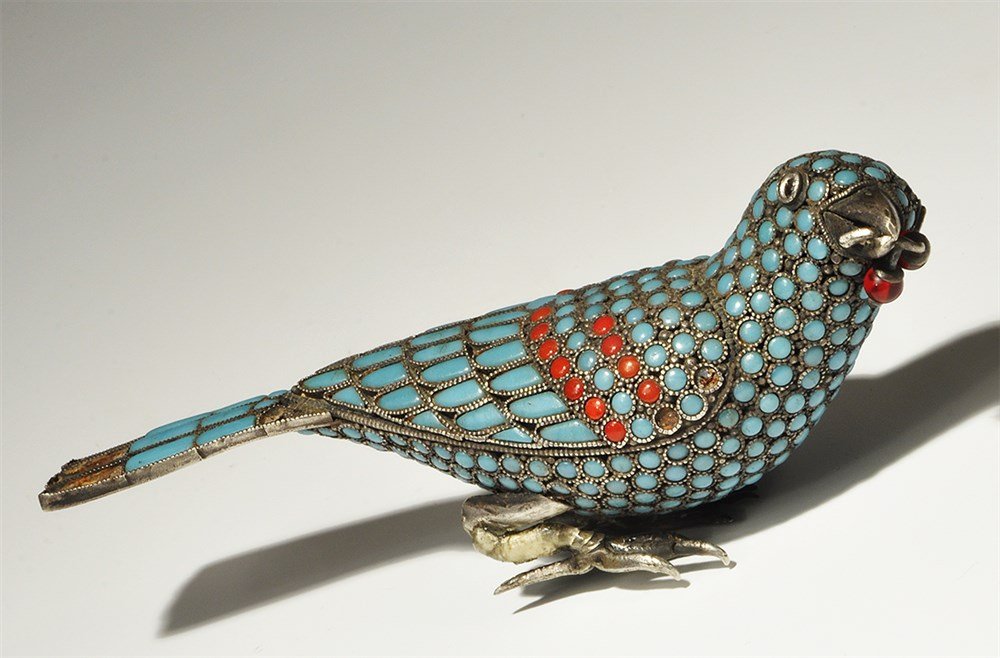 Islamic Silver Turquoise-Inlaid Bird Figurine: An undated archaistic hollow bird figurine with discoid and tongue-shaped turquoise inserts, red stone inserts to the upper wings; in the beak a twig with two red glass cherries. 115 grams, 12.5 cm (5