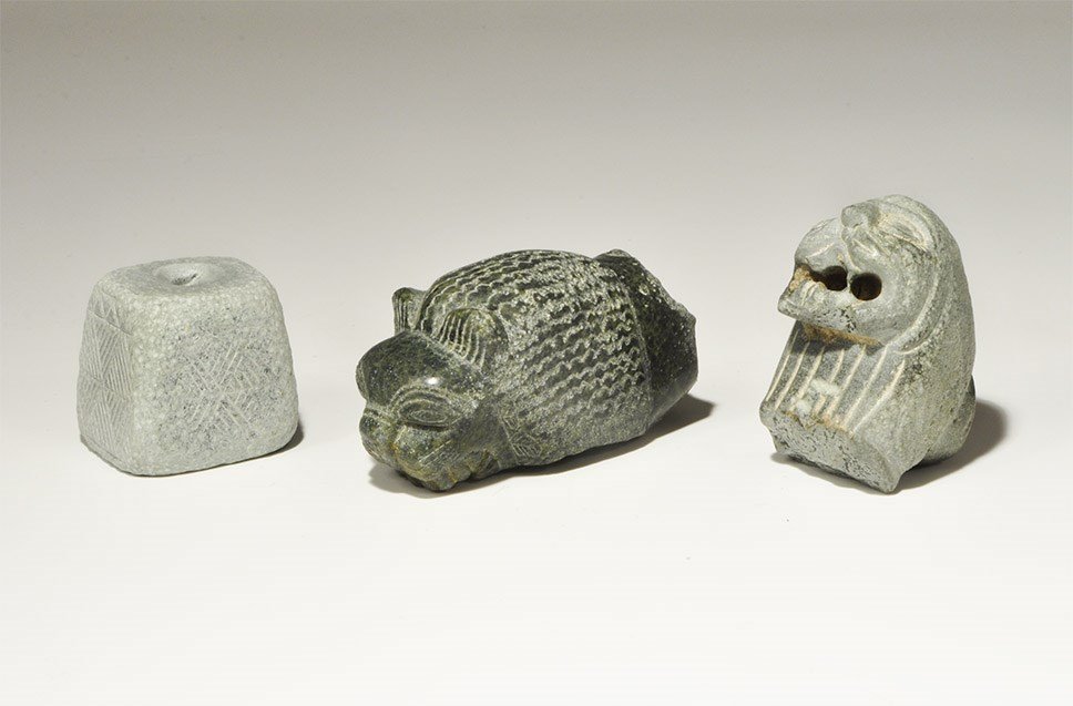 Islamic Style Carved Stone Group: A mixed group of undated archaistic carvings comprising: a serpentine feline head and neck with bared teeth; a soapstone feline head with pierced mouth; a trapezoidal soapstone idol with hatched motif