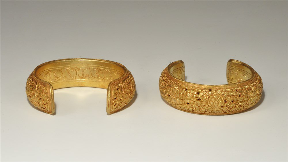 Chinese Tibetan Style Silver-Gilt Bracelet Pair: A pair of undated archaistic penannular bracelets, each with incised running-scroll ornament to the inner face, high-relief foliage to the outer face, beaded border. 130 grams total, 80 mm diameter ea