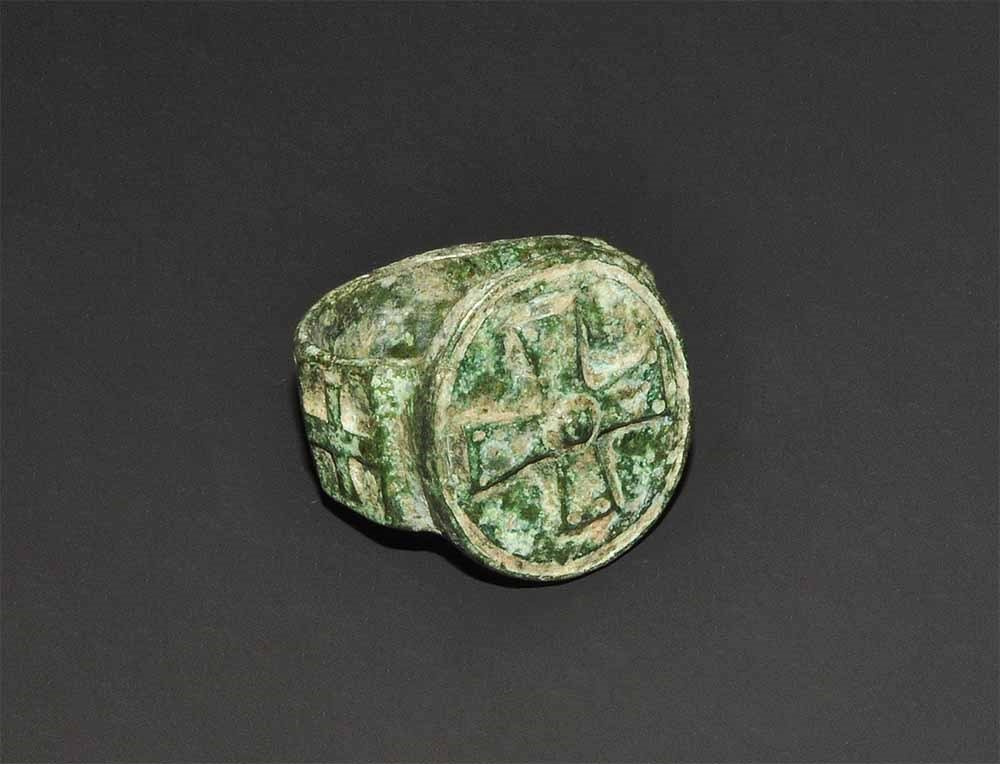Byzantine Bronze Ring with Expanding Cross: 6th-9th century AD. A flat-section hoop with the panels to the shoulders, each with a raised cross motif, the bezel discoid with raised expanding-arm cross, central pellet. 16 grams, 25 mm overall, 18
