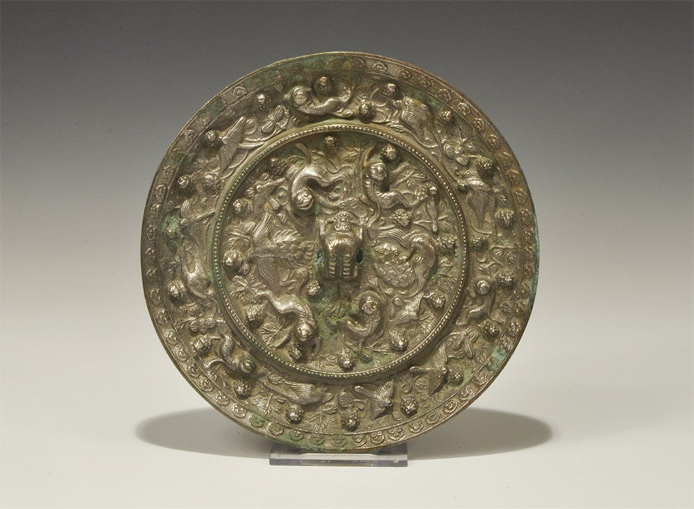 Chinese Style Bronze Mirror with Monkeys: An undated archaistic discoid mirror with one polished face; to the reverse a central pierced lug surrounded by monkeys and bunches of grapes. 815 grams, 16 cm (6 1/4"). Acquired on the London art mar