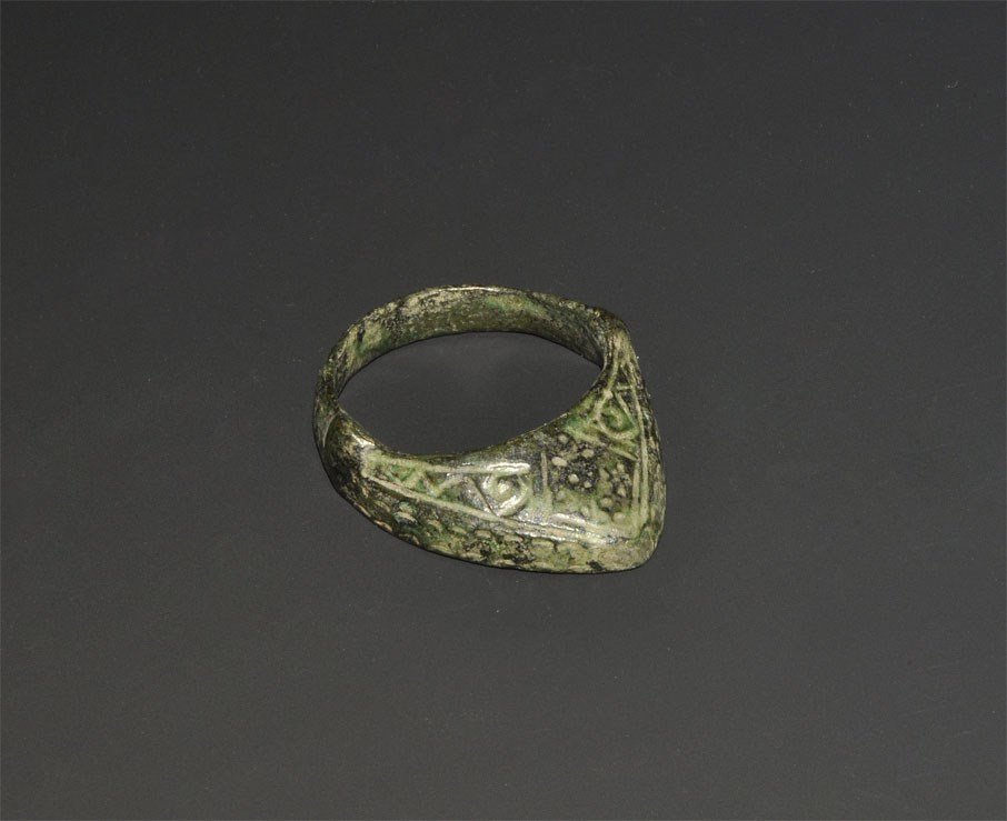 Byzantine Bronze Archer's Ring: 10th-14th century AD. A cast thumb ring with lateral flanges and triangular extension decorated with incised scrolled linear designs and central lozenge panel. 11 grams, 41 mm overall, 24.35 mm intern