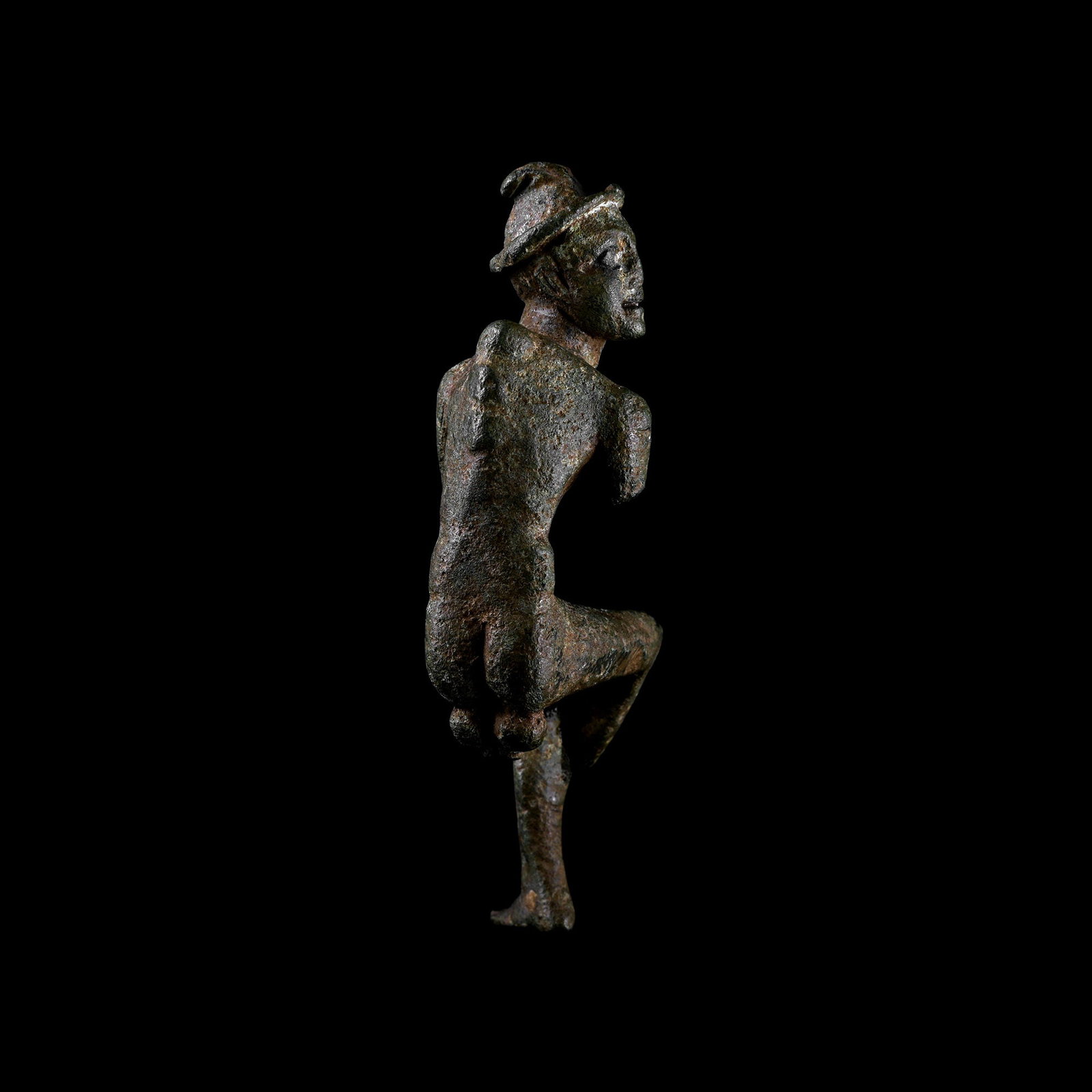 Roman Bronze Hunchback Grotesque Statuette: 1st century B.C.-1st century A.D. Modelled in the round, sitting nude with head turned, arms and legs bent; wearing a brimmed cap with a feather in the crown; the spine and sternum modelled protruding