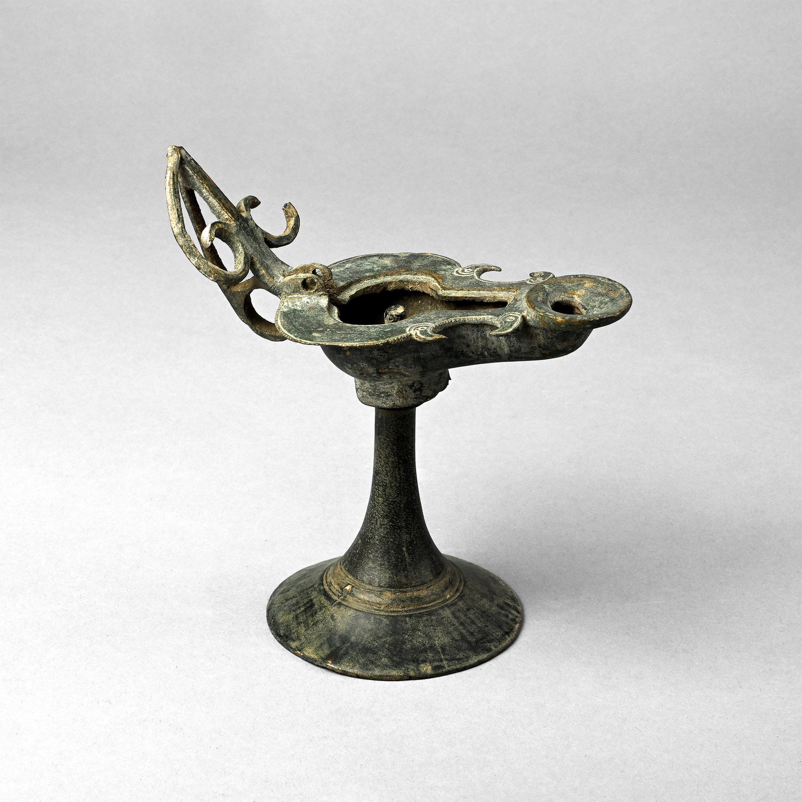 Late Roman Bronze Lamp and Stand: Circa 5th-6th century A.D. Comprising a slipper-shaped lamp with broad flange rim to the shoulder and rear with hooked spurs; scooped recessed nozzle; handle to rear formed as a vertical bar with late