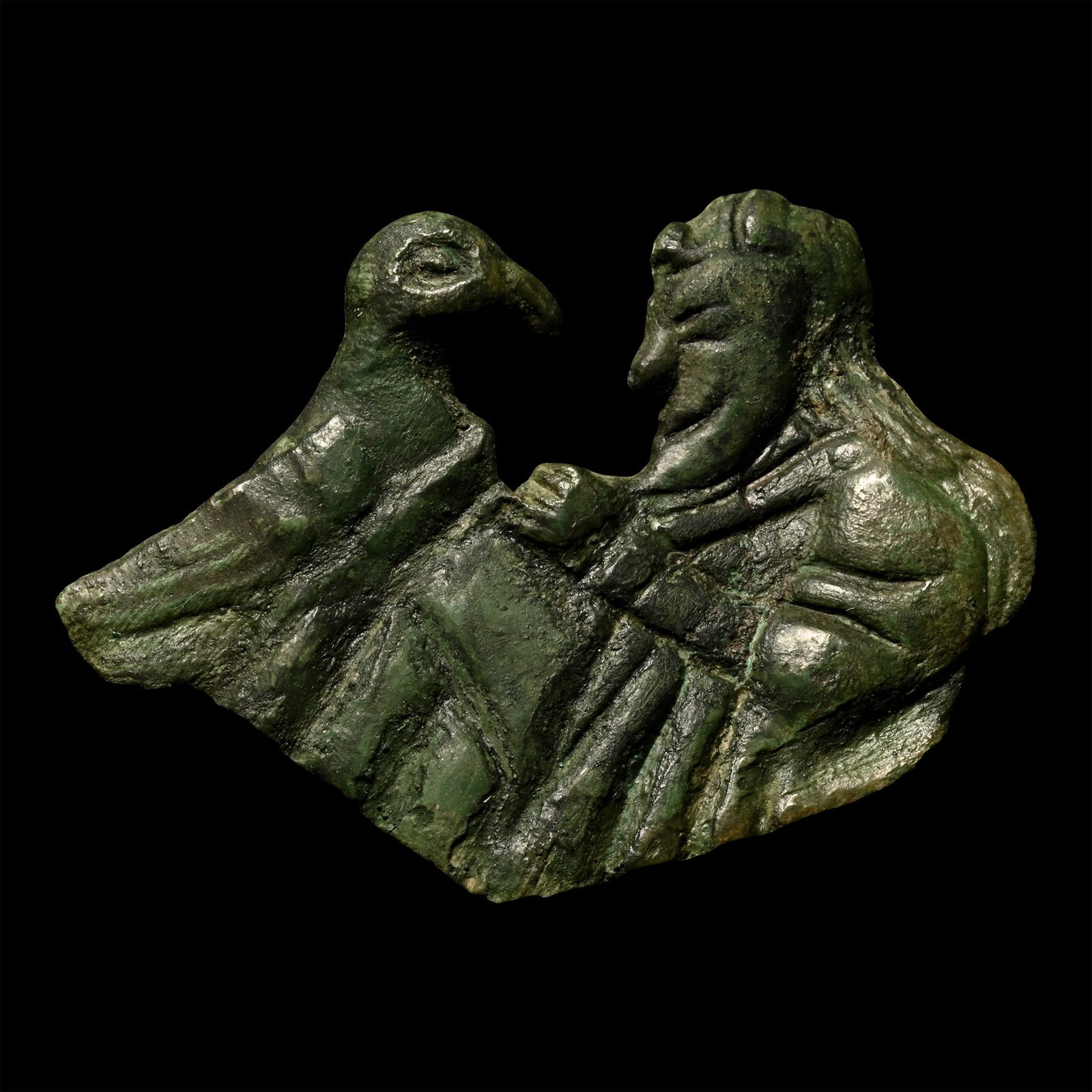 Viking Bronze 'Wayland the Smith' Mount: Circa 10th century A.D. Depicting a male figure with almond-shaped eye, pointed curved chin, small nose, long hair with a curl above the forehead; dressed in a loose short-sleeve tunic(?), with hands 