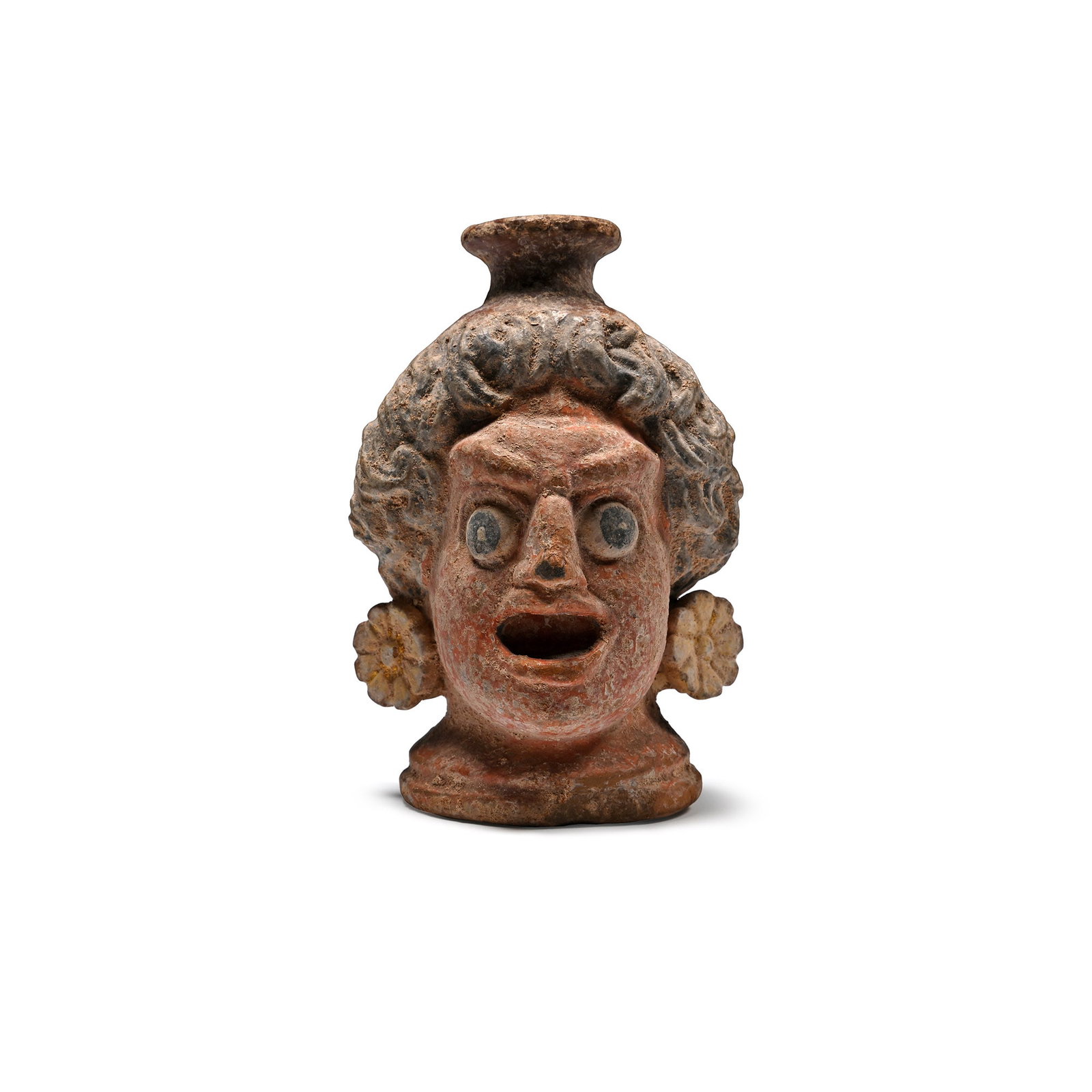 Greek Terracotta Head of an Actor Vase: Circa 4th century B.C. An expressive polychrome vase formed as the head of an actor wearing rosette earrings, open mouth and applied pupils, short neck with everted rim above and a small strap handle 