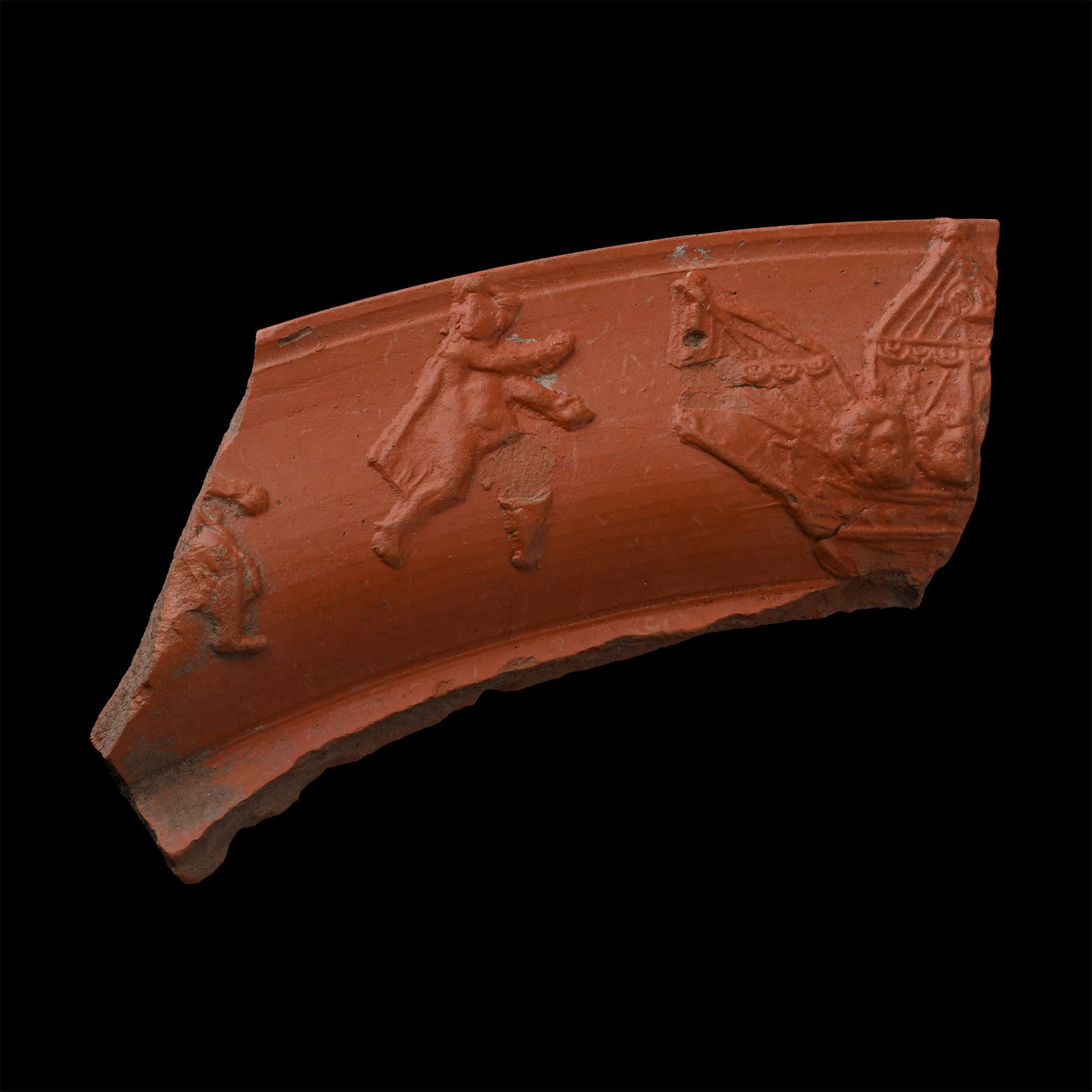 Roman Red Ware Platter Fragment with Ship and Figures: Circa 3rd-4th century A.D. A thick rim fragment from a shallow platter showing an oneraria ship with open sails and two profile heads facing right, a nude figure at the centre in a dynamic pose, weari