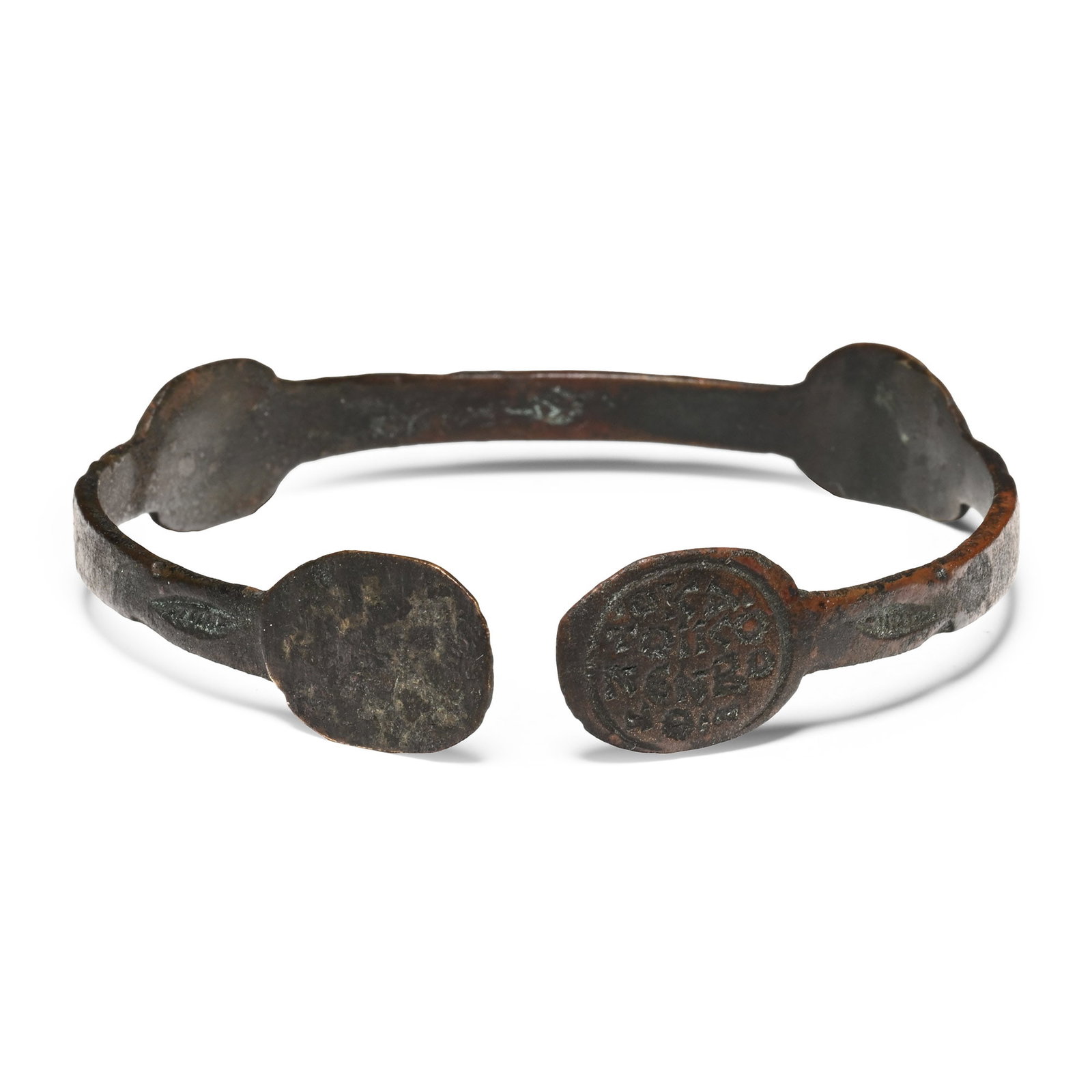Byzantine Bronze Bracelet with Saints and Inscription: Circa 6th-8th century A.D. Penannular band with discoid lobes and finials, punched leaf motifs; impressed nimbate saint on galloping horse; two nimbate saints flanking a throne; legend '·OKA· TO?CO 