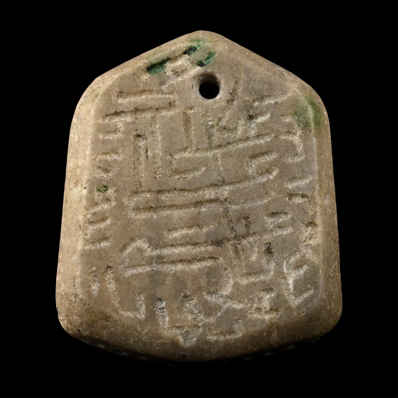 Western Asiatic Stone Talisman Pendant: Circa 9th-13th century A.D. Hexagonal in plan with rounded sides ornamented with a row of roundels, holed at the top; inscribed legend to both faces. 51.9 grams, 51 mm (2 in.). [No Reserve] Formerly i