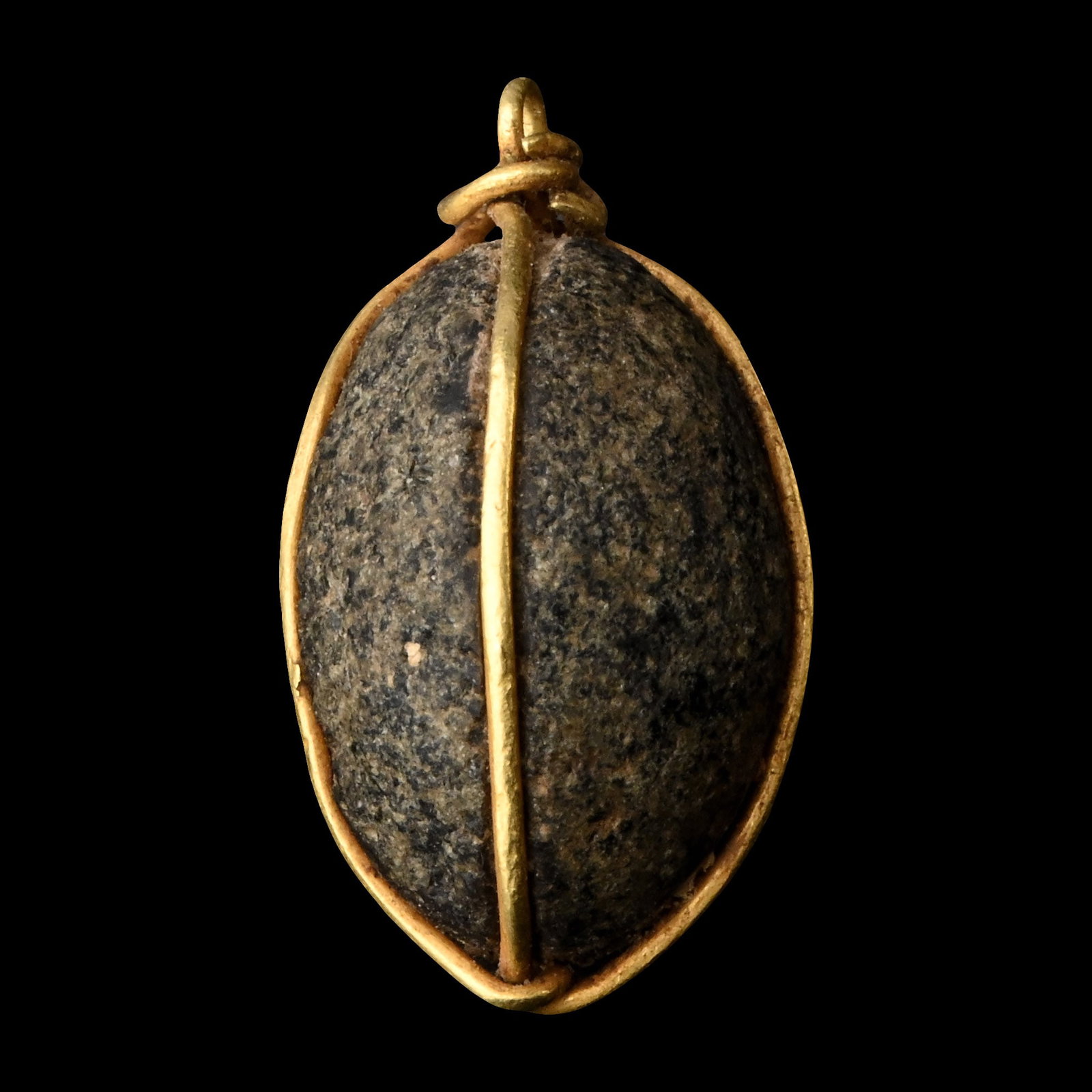 Western Asiatic Bead with Gold Wire Pendant: Early 1st millennium A.D. A seed-shaped black stone pendant with grooves to accept a gold wire wrapped around the body with a loop above. 2.12 grams, 18 mm (3/4 in.). [No Reserve] From the private col