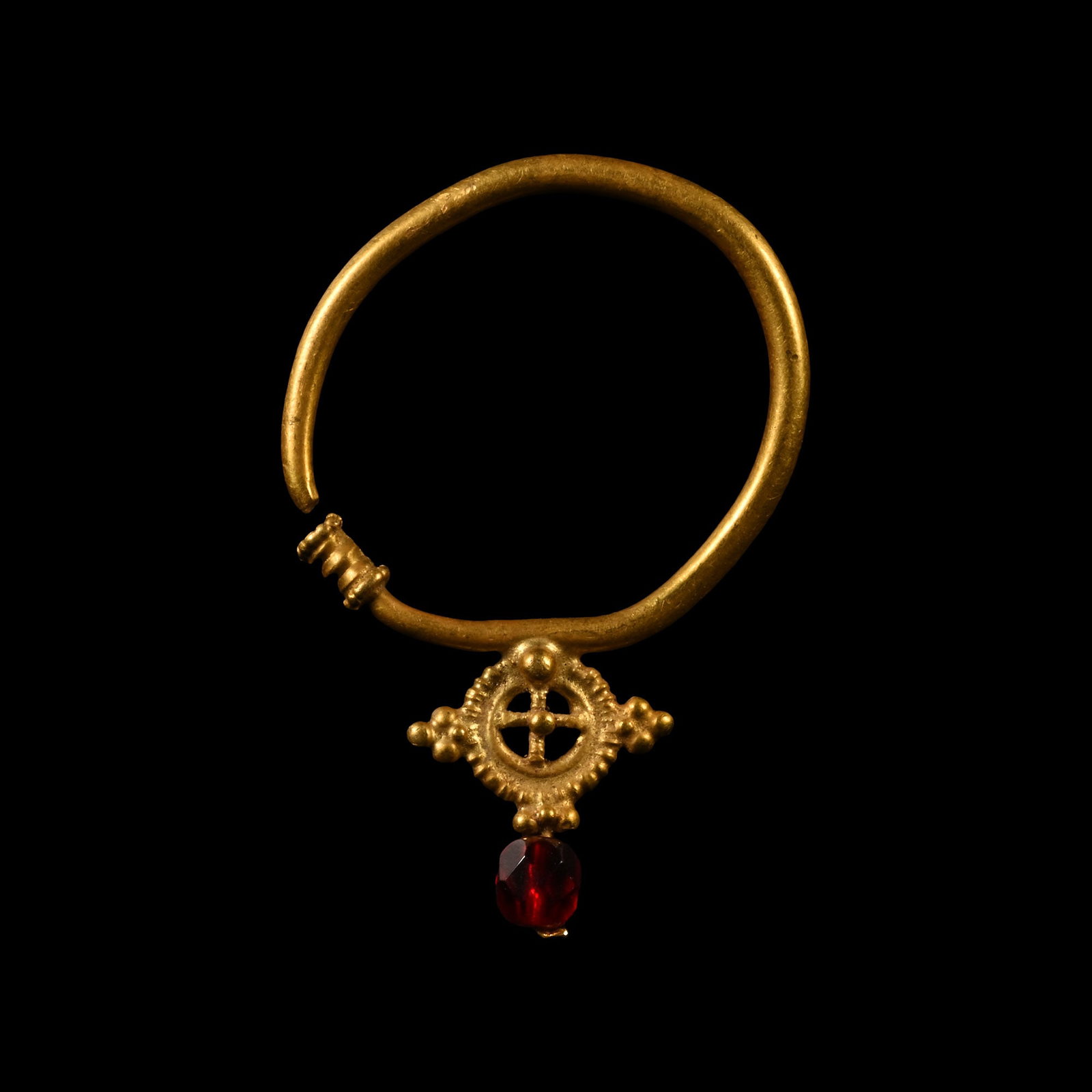 Post Byzantine Gold Earring with Cross and Garnet: Circa 17th-18th century A.D. Penannular hoop with applied collars, applied discoid plaque with beaded rim and openwork cross to the centre, lateral granule clusters, facetted garnet bead below. 6.53 g