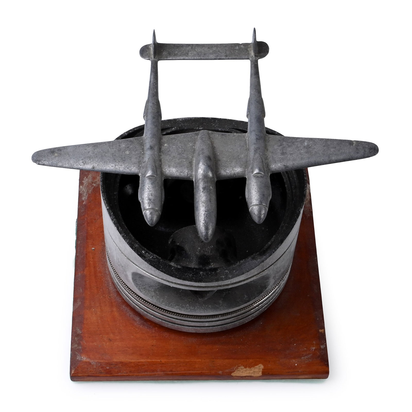 American Air Force WWII Fighter P38 Lightning Engine Piston: 1939-1945 A.D. Aluminium cast model of a P38 Lightning fighter aircraft mounted on a spigot in the centre of a piston casing; on a wooden stand. 1.88 kg, 17 cm high (6 5/8 in.). [No Reserve] Acquired 