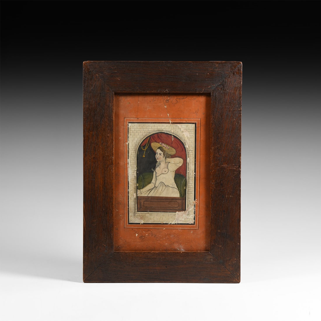 Indian Framed Watercolour Painting: 20th century A.D. A rare watercolour painting showing a European woman seated in a bed against a cushion framed by an open window, wearing a hat and a dress pulled down at the chest exposing her breas