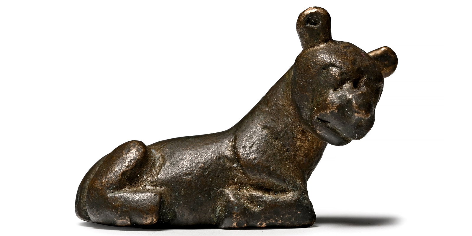 Western Asiatic Bronze Reclining Cat Weight.: Early 1st millennium AD. Modelled in the round with neck and head extended, legs folded beneath the body 21.91 grams, 35.36 mm (1 3/8 in.). Ex London, UK, gentleman's collection by descent, 1980s. Tim