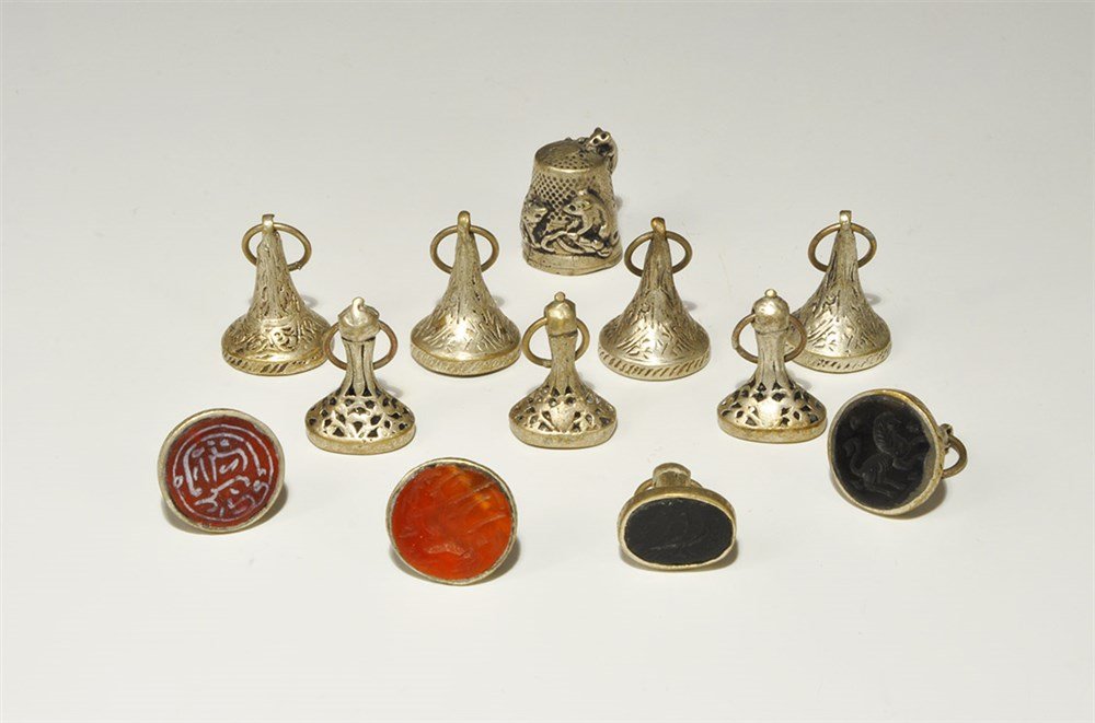 Islamic Style Silver and Stone Seal Group: A mixed group of undated archaistic stone stamp seals in conical silver settings; the motifs comprise seven quadrupeds, two calligraphic text blocks, two birds; offered with a thimble with miniature m