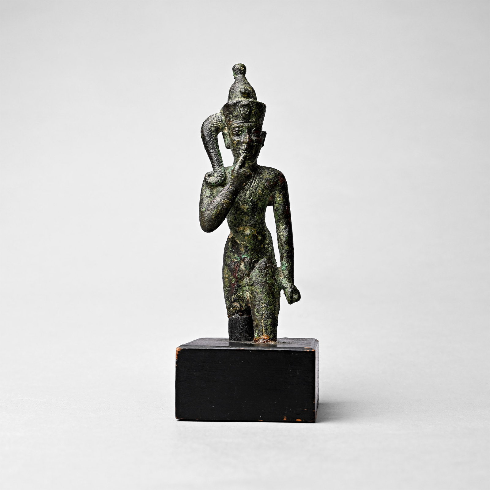 Egyptian Bronze Statuette of Young Horus: Late Period, 664-332 B.C. Modelled in the round in striding pose with one arm resting along the body and the right hand raised to his mouth, wearing an elaborate side-lock of youth and Pschent crown f