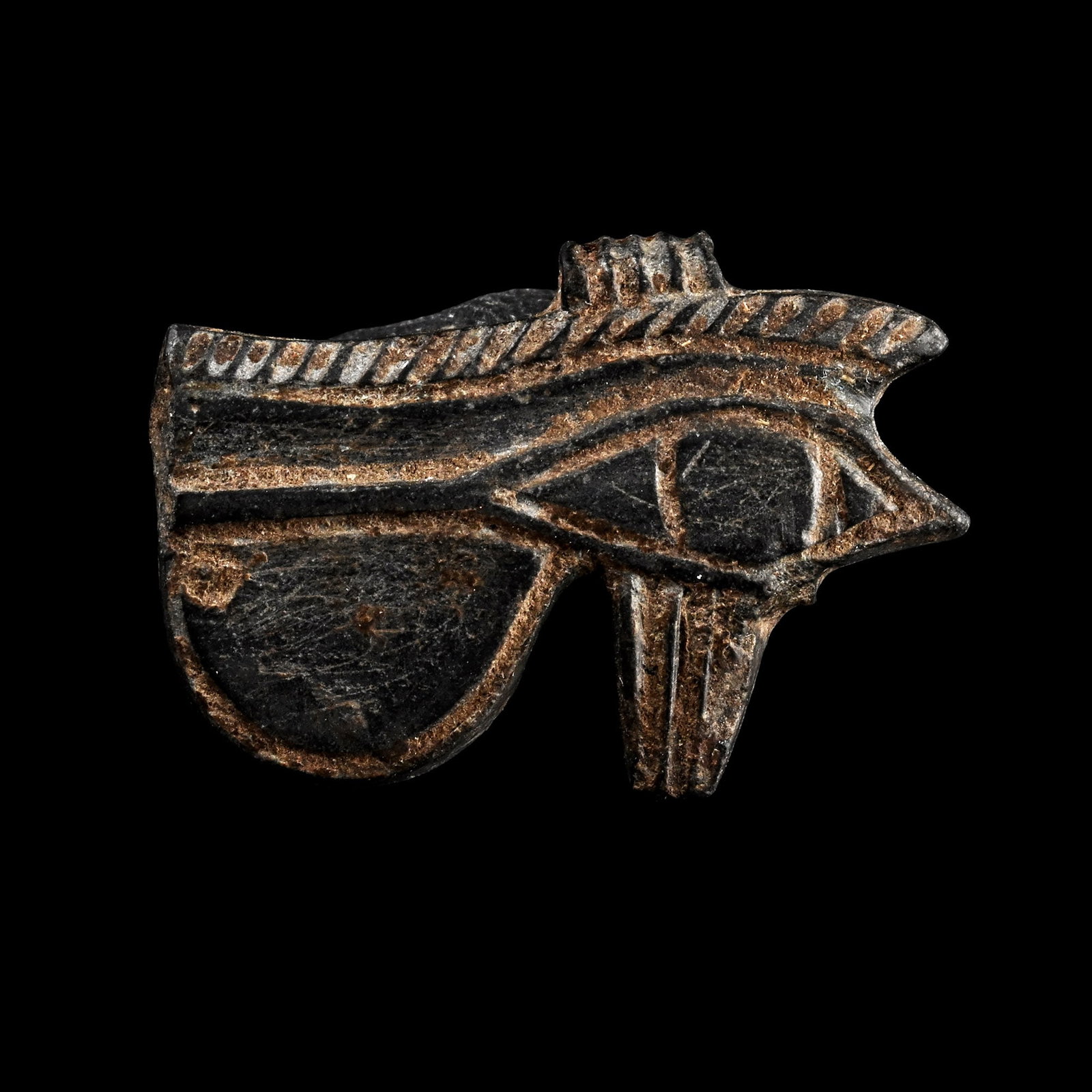 Egyptian Black Steatite Eye of Horus Amulet: Late Period, 664-332 B.C. Carved unifacial amulet with hatched eyebrow and ribbed suspension loop. Cf. Flinders Petrie, W.M., Amulets, London, 1994, pl.XXV, fig.138l, for type. 1.45 grams, 19 mm (3/4 