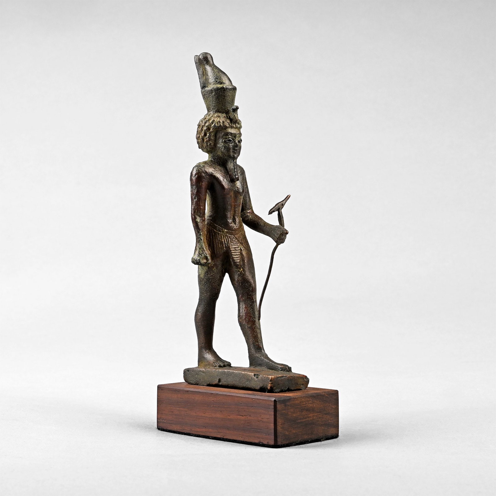 Egyptian Bronze Statuette of the God Neferhotep: Ptolemaic Period, 332-30 B.C. Neferhotep depicted advancing on a rectangular base, holding in the left hand the was sceptre, topped with the stylised head of an animal linked to the god Seth, with the