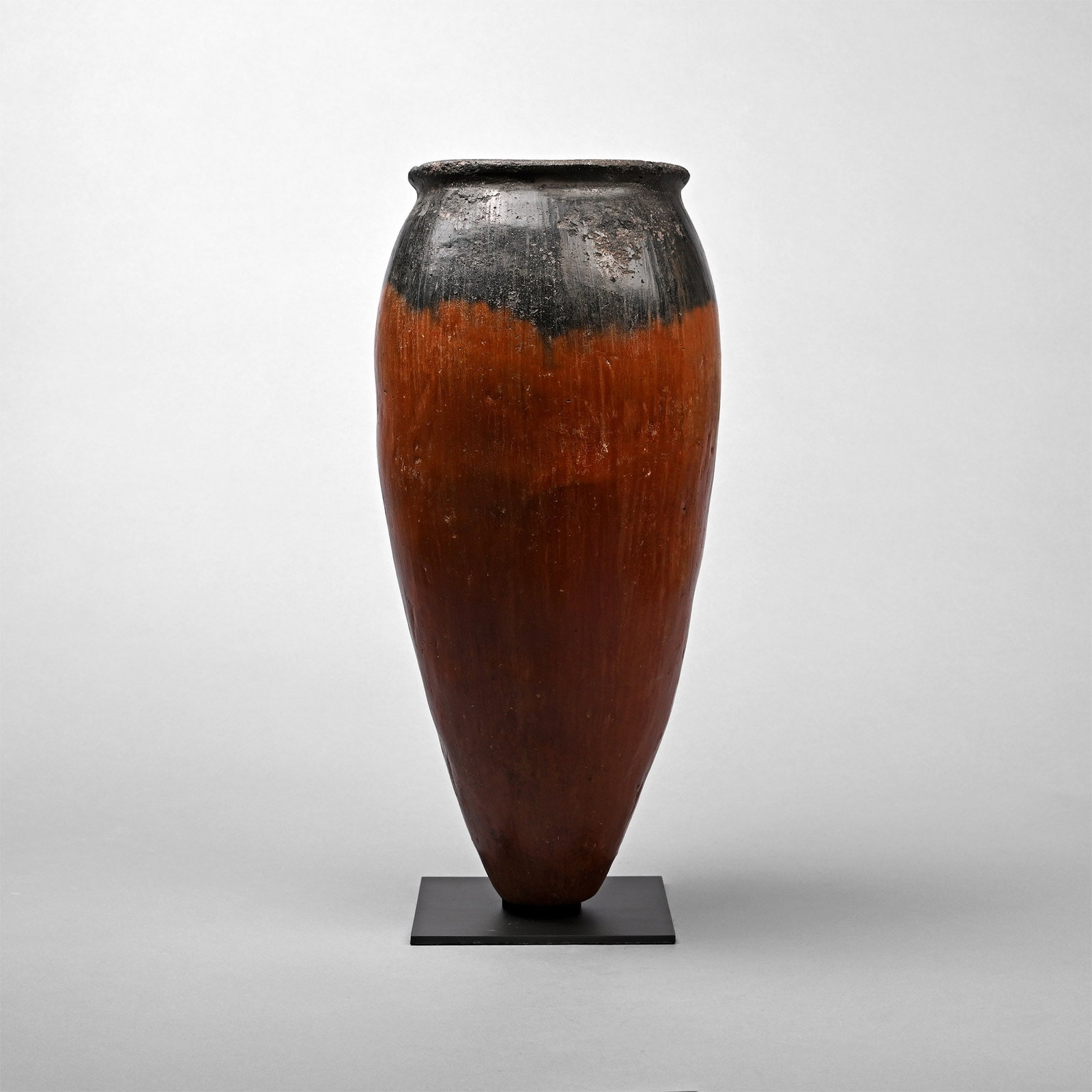 Very Tall Egyptian Black-Topped Vase: Predynastic Period, Naqada II, circa 3900?3400 B.C. A finely made, coil-formed Nile silt clay, red-polished pottery vessel with elongated ovoid body, pointed base, rounded shoulder, and narrowing neck