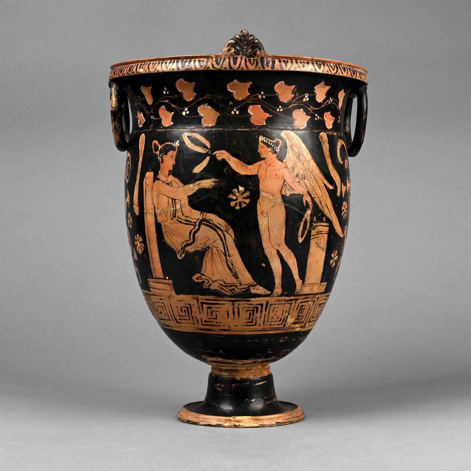 Greek Red-Figure Bell Krater with Eros: Apulia, 4th century B.C. With flared and carinated foot, broad stem, ovoid body, carinated shoulder, everted rim with lip, D-shaped antefixes and lateral pendant loop handles; band of ivy to the neck 