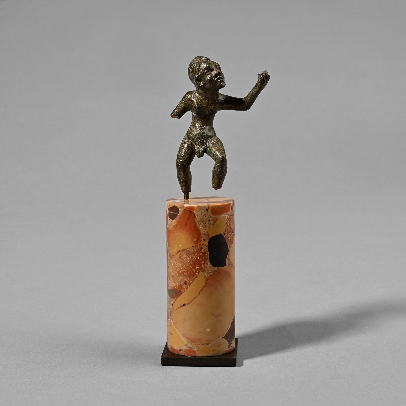 Greek Bronze Statuette of an Alexandrian Dancing Dwarf: Hellenistic, 1st century B.C.-1st century A.D. In an active pose with both legs bent and left arm raised dramatically, head tilted to the left; exaggerated facial features, short trimmed hair, slim bo