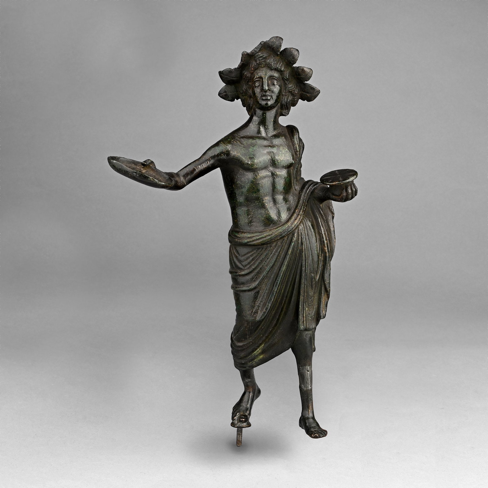 Large Etruscan Statue of a Priest with Patera: 2nd century B.C. Modelled in the round standing figure with palla draped over the left shoulder and from the hips, extending to calf-length; the head with aquiline nose and dimpled chin modelled with 