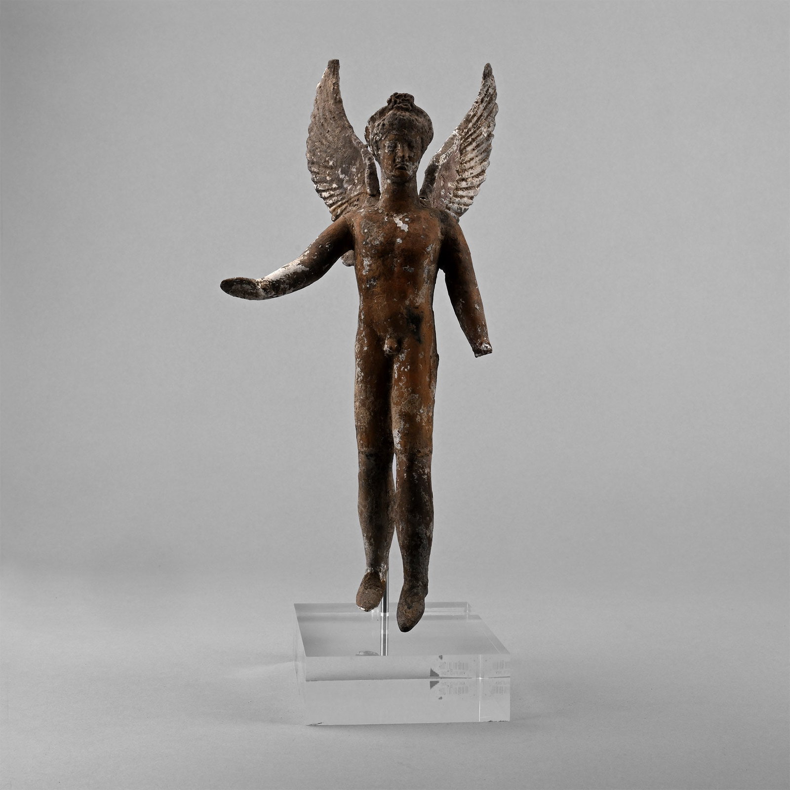 Greek Terracotta Figure of Eros, the God of Love: Hellenistic, 3rd-1st century B.C. Modelled nude in a dynamic pose with his wings spread open, the left leg slightly advanced, and the right arm extended with open palm, a diadem or a fillet on his hea
