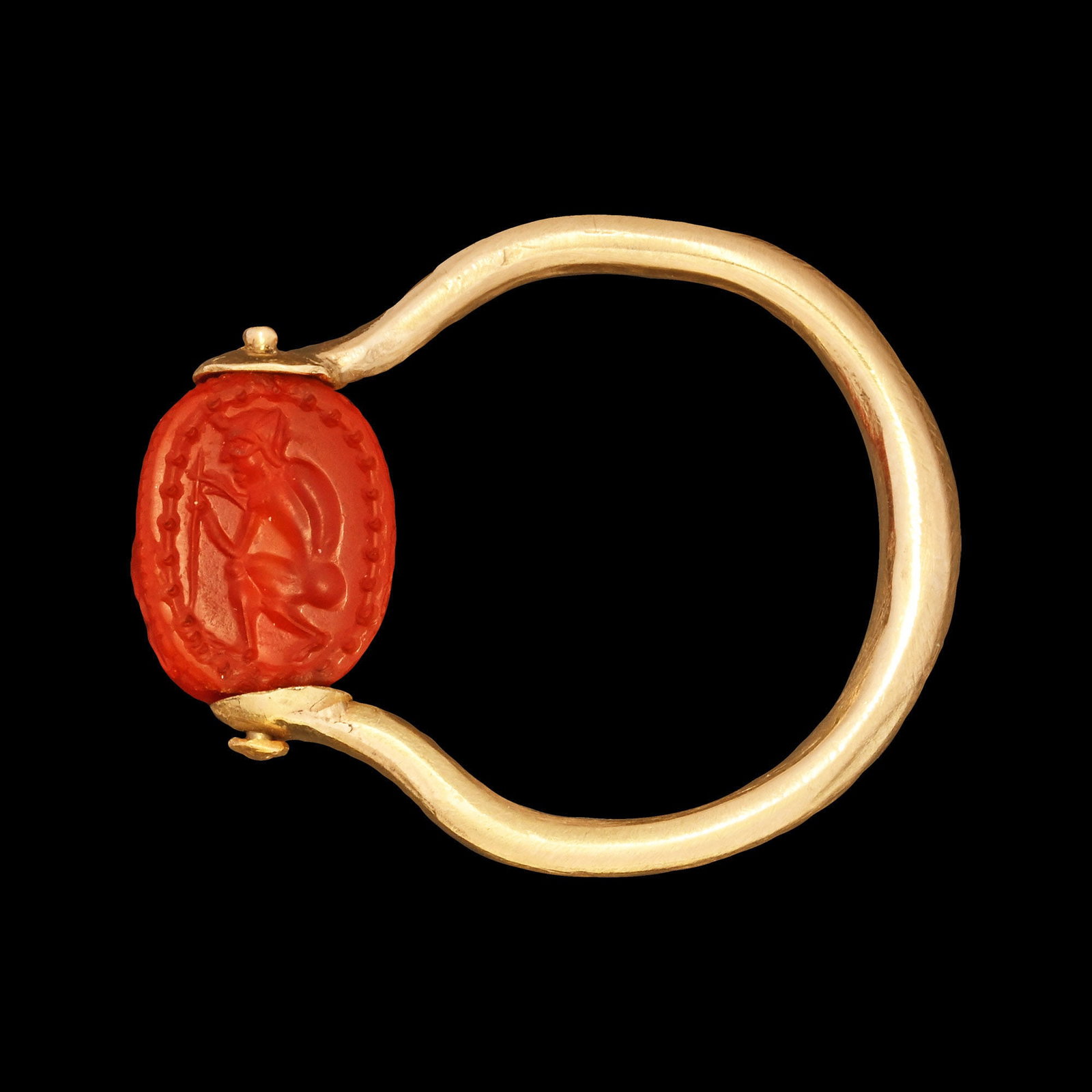 Etruscan Carnelian Scarab of a Fletcher in Gold Ring: Late 4th-3rd century B.C. With carapace detailing and intaglio of a crouching male carving an arrow, set within a dotted border; set into a later gold swivel ring. For the motif, see Boardman, J. and 