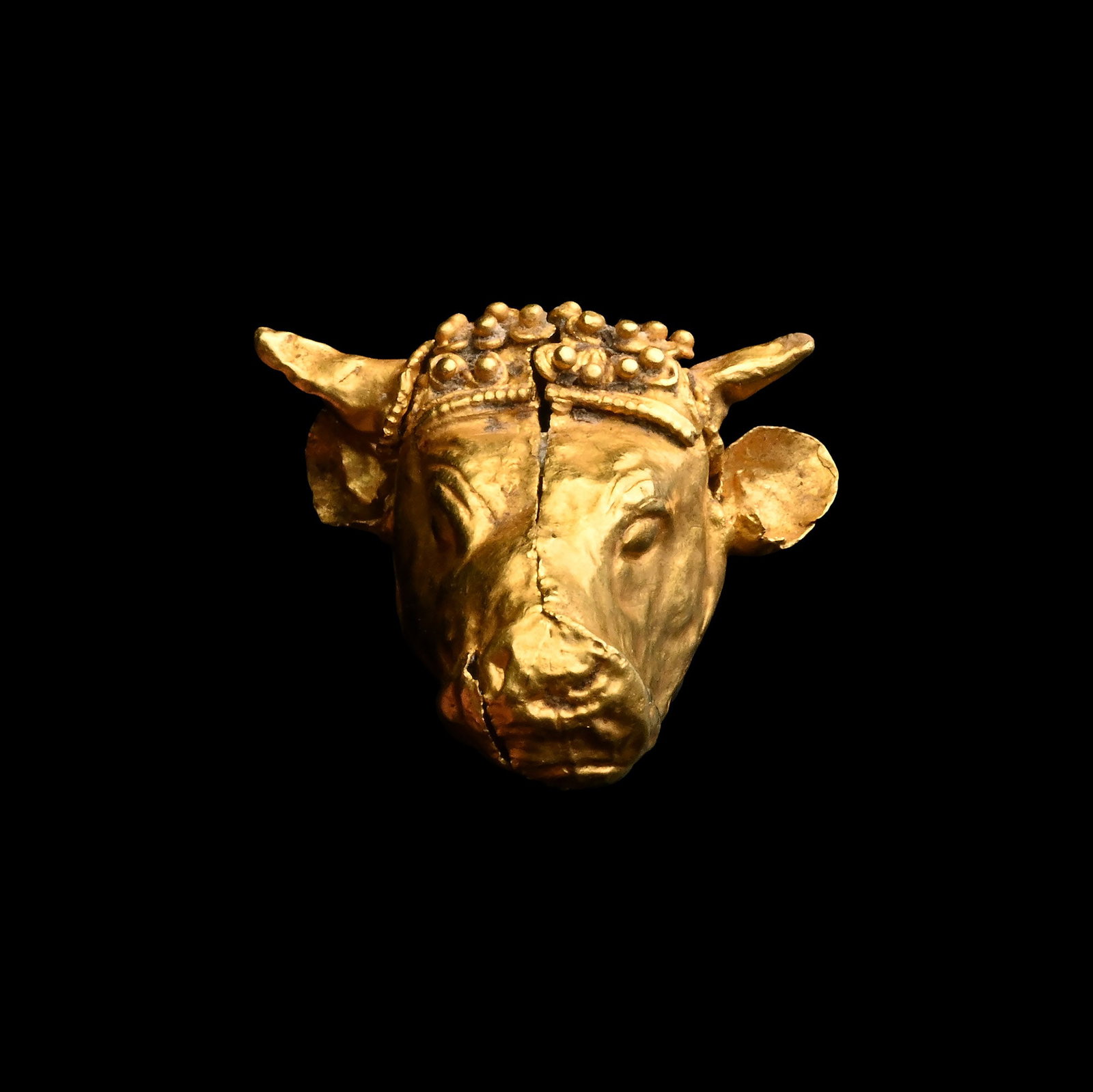 'The Mildenberg' Greek Gold Bull's Head Pendant: Circa 4th century B.C. Hollow-formed in sheet gold with finely modelled details and applied granulated wreath between its horns; attachment hole to the rear of the head. Cf. similar bull-head pendant 