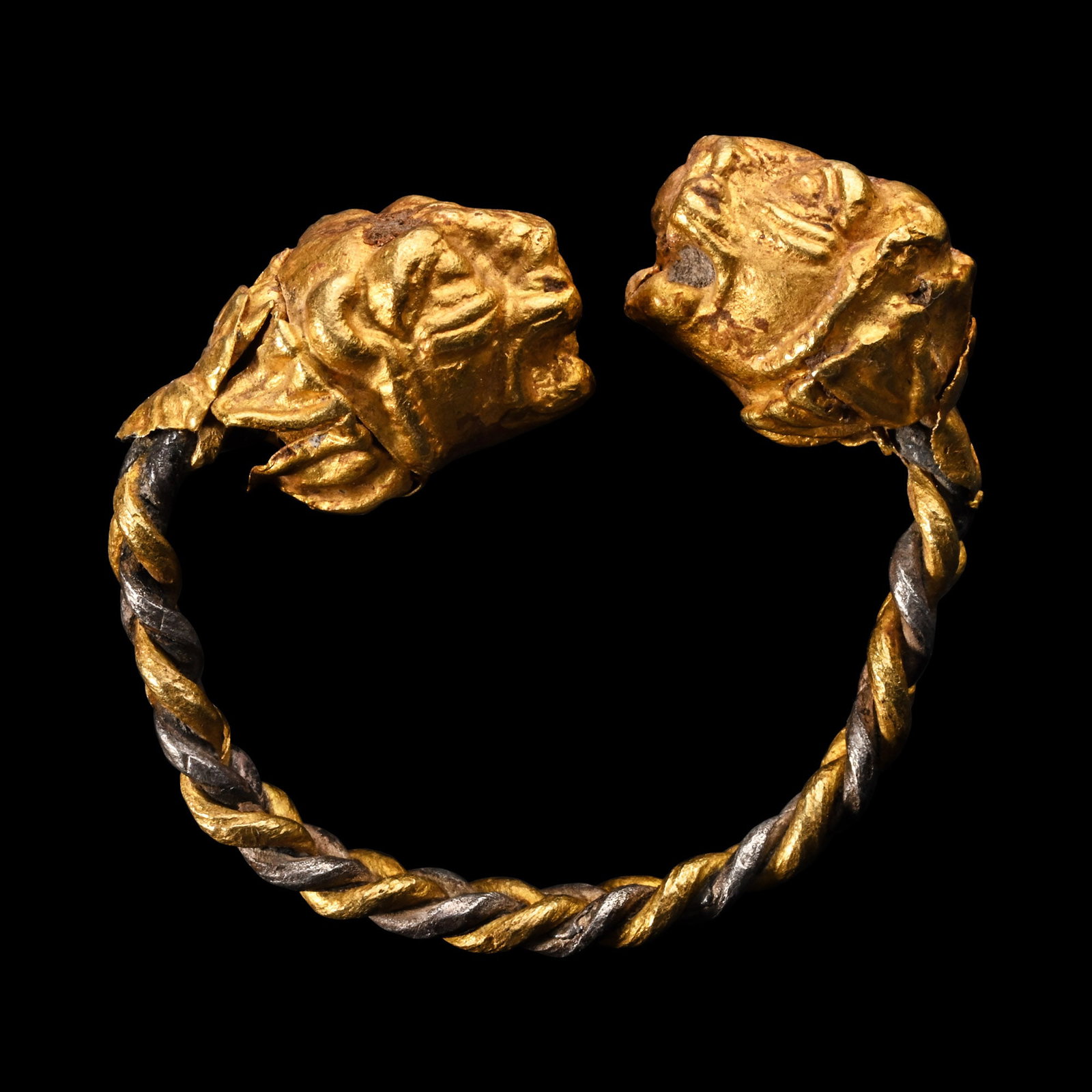 Greek Gold Lion Head Ring with Plaited Band: 3rd century B.C. and later Formed as a plaited band of gold and silver rods, the finials formed as large lion heads with gaping jaws, a rosette with a rivet behind the neck; possibly a marriage. 8.43 