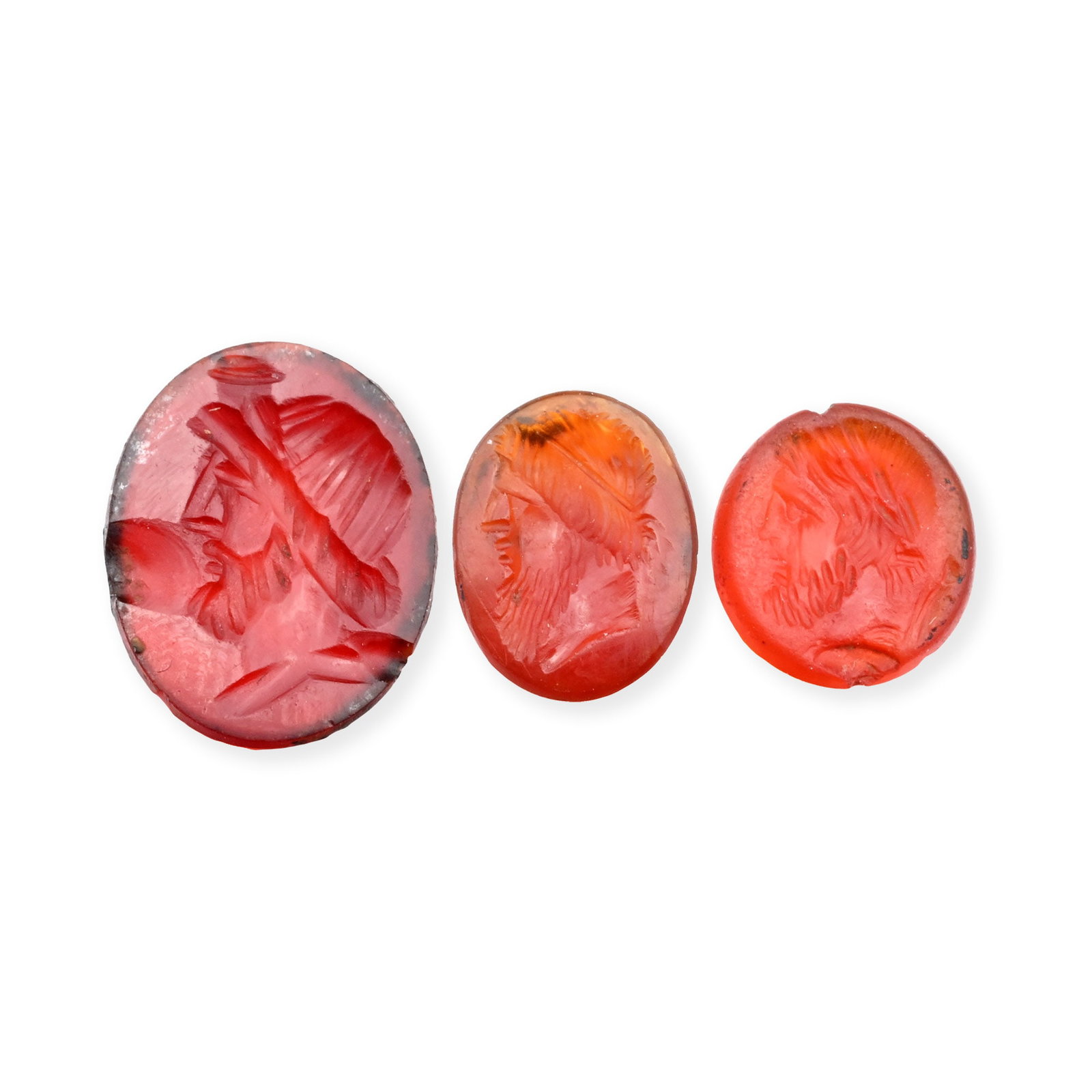 Roman Carnelian Gemstone Collection with Jupiter Effigies: 1st century B.C. Comprising three oval intaglios, one with a domed base and each featuring a profile bust, one wearing a modius and one wearing a laurel wreath; supplied with museum-quality impression