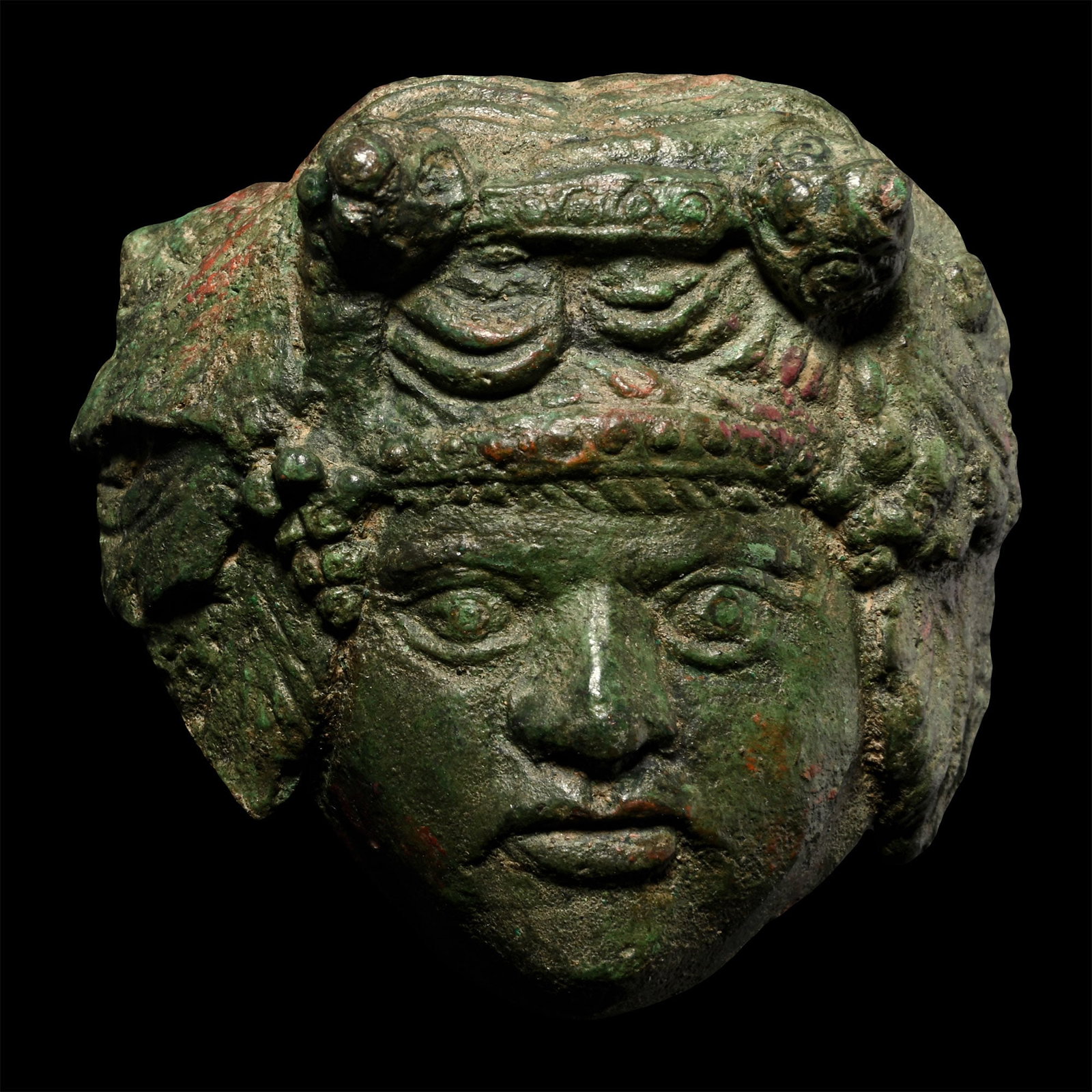 Roman Bronze Head of Dionysus Mount: 1st-2nd century A.D. Large convex mount depicting the head of the god of wine, shown facing with rounded cheeks and staring eyes, large vine leaves with bunches of grapes framing his face; ferrous spi