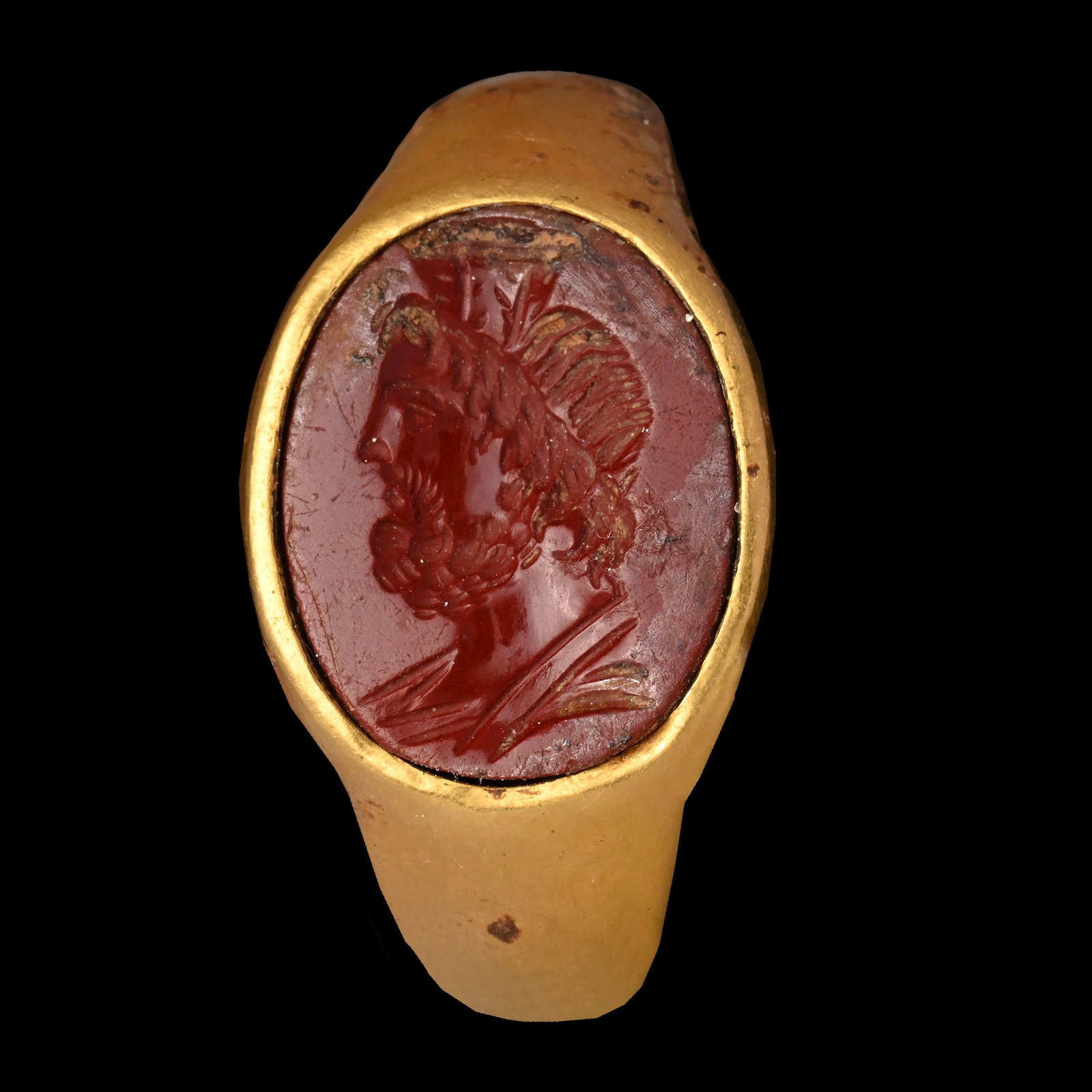 Roman Gold Ring with Bust of the God Serapis: 1st-2nd century A.D. Hollow-formed hoop with broad ellipsoid cell, inset red jasper intaglio profile bust of Serapis with modius; possibly a marriage, supplied with a museum-quality impression. Cf. Ch