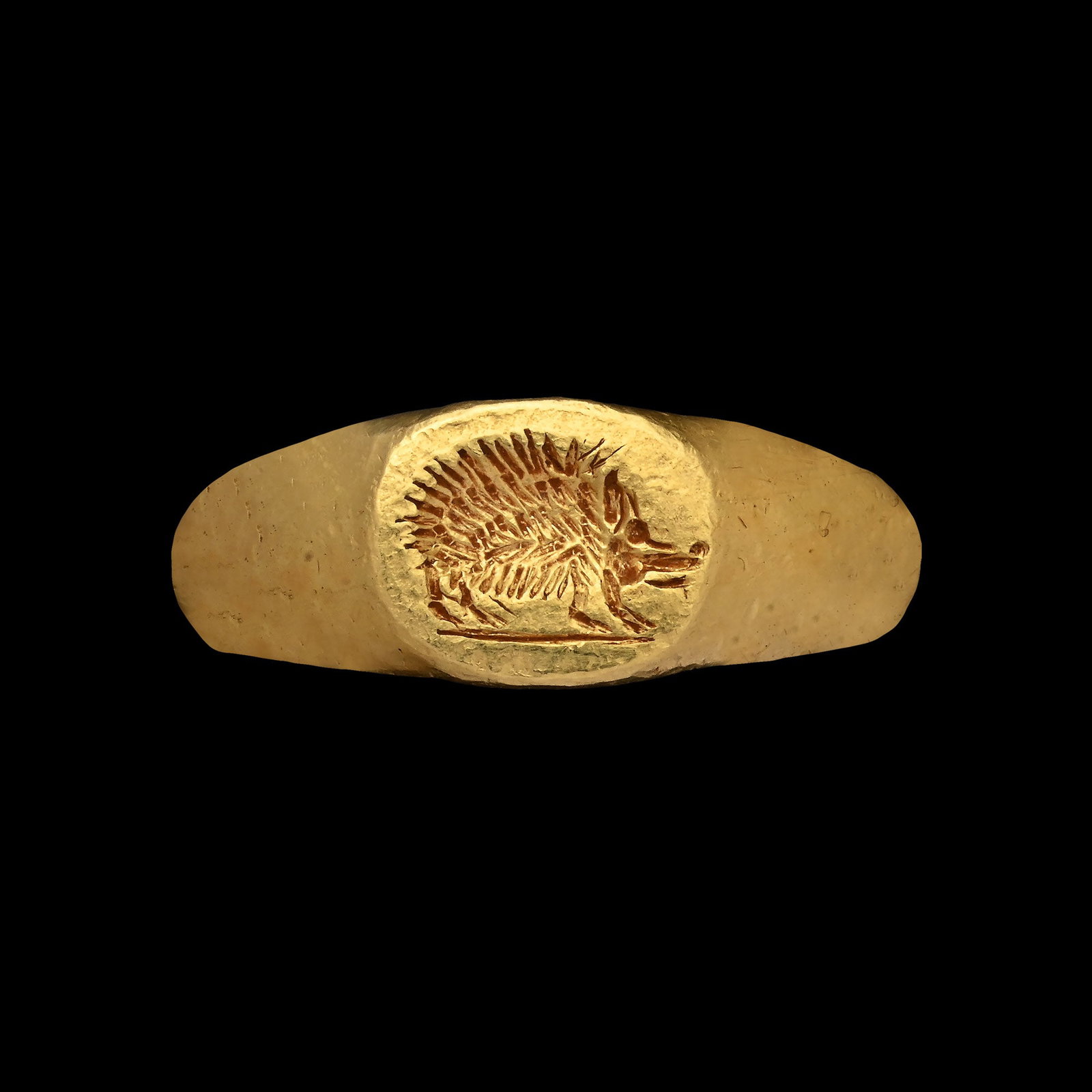 Roman Gold Ring with Carved Hedgehog: 1st century B.C. Comprising a thick hoop expanding at the shoulders, the bezel with a standing hedgehog on a baseline with detailed spines. 7.53 grams, 20.12 mm overall, 15.03 mm internal diameter (ap