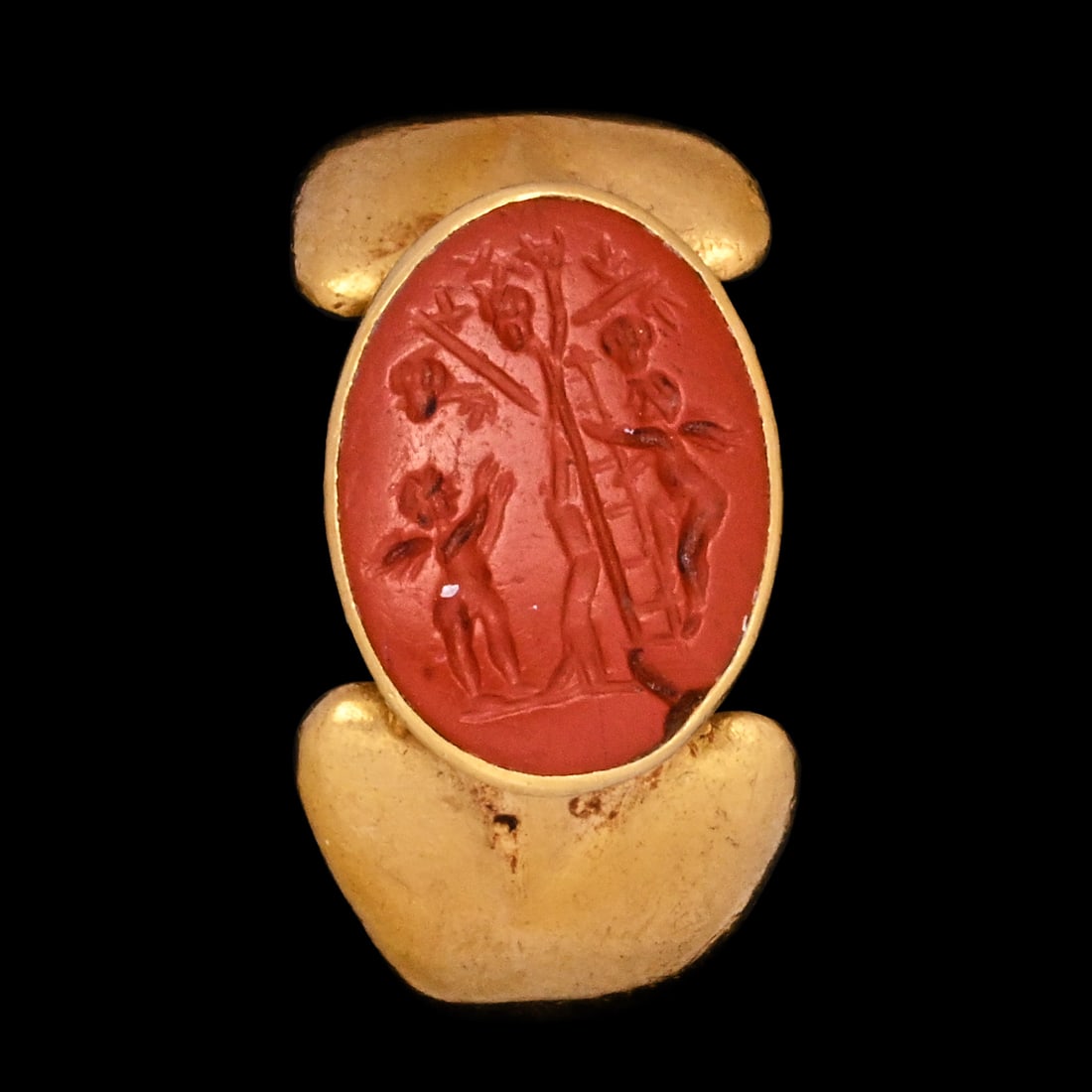 Roman Red Jasper Gemstone with Group of Amores Harvesting Grapes in Gold Ring: 1st-2nd century A.D. The hoop with flaring shoulders and an oval bezel set with a jasper intaglio engraved with a winged Amore (Erote) standing beneath a tree bearing grapevines, another Amore climbin