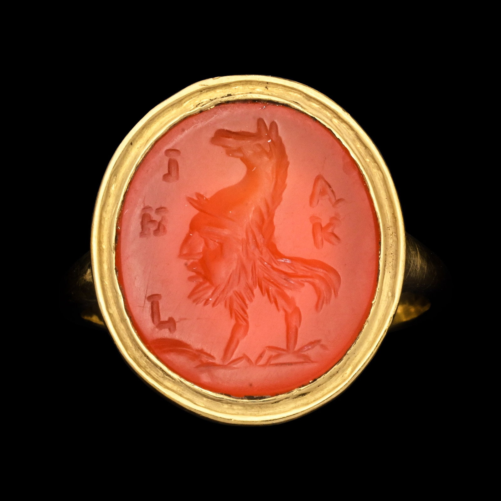 Roman Carnelian Gemstone with Gryllus in Gold Ring: 2nd century A.D. Translucent oval intaglio featuring a standing gryllus wearing a gryphon-headed helmet, flanked by the inscription 'KA?HI' meaning 'to the beautiful one'; set in a later gold ring wit