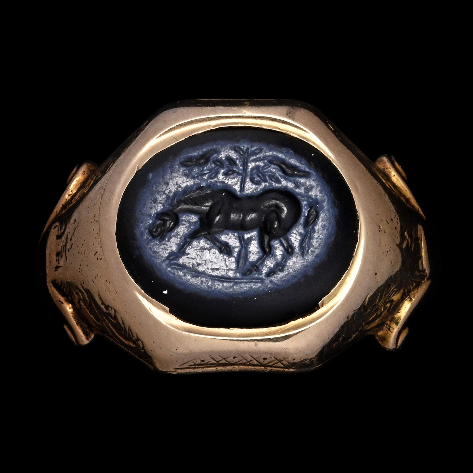 Roman Nicolo Intaglio Depicting a Horse Beneath a Tree in Gold Ring: 1st century A.D. Comprising a dark blue layered chalcedony, engraved with the figure of a horse standing beneath a stylised tree, within which perch two birds, mounted in a later gold ring of broad, f
