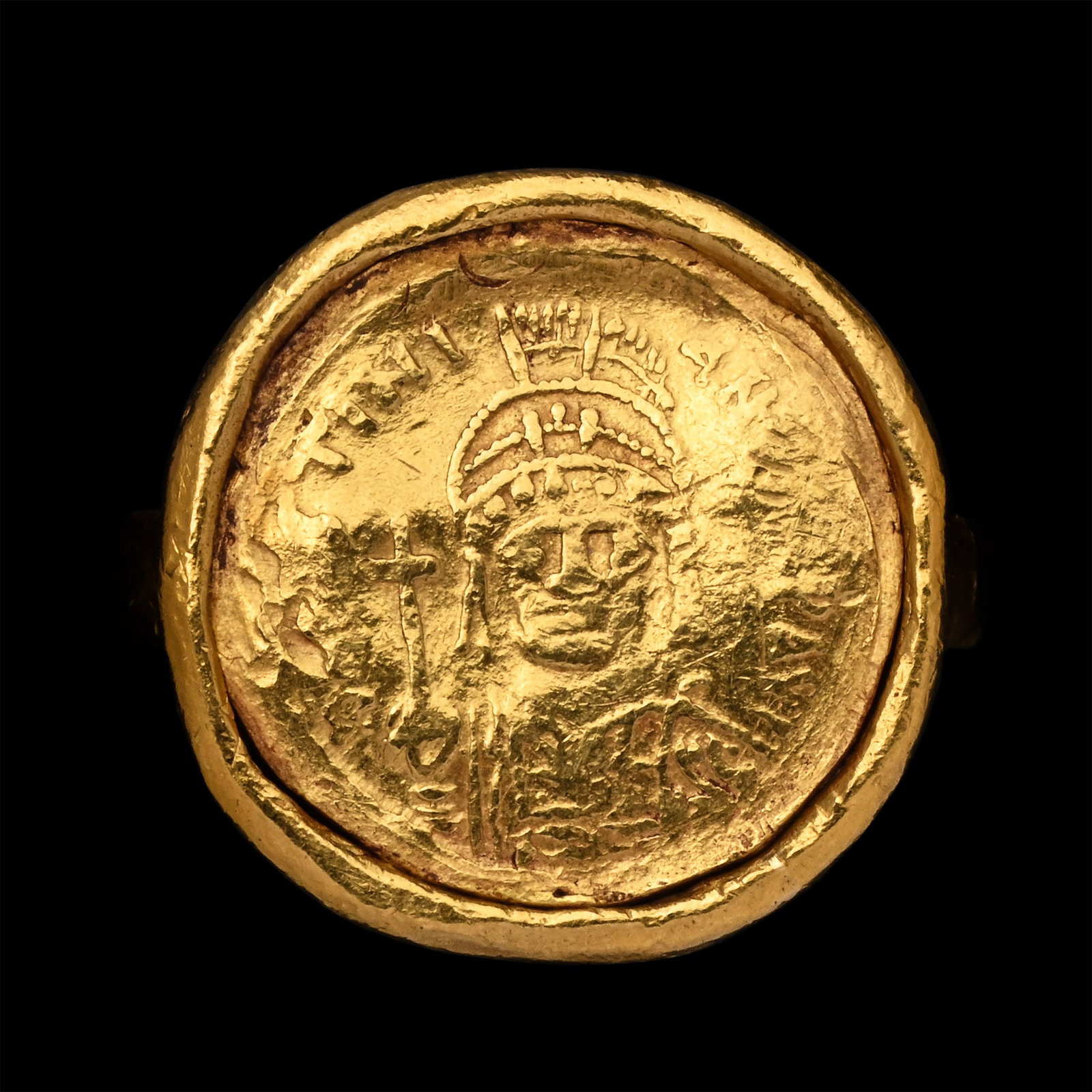 Byzantine Gold Solidus in Gold Ring: 6th century A.D. The coin showing a facing bust of a pearl-diademed emperor, cuirassed and holding a cross; set in a thick frame with a double rectangular-section hoop below; the solidus a cast or bar