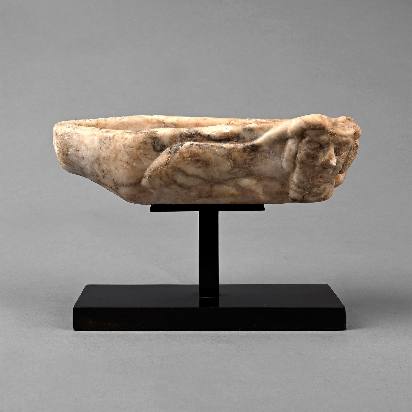 Old Babylonian Alabaster Vessel with Recumbent Lamassu: Early 2nd millennium B.C. Deep elongated vessel, carved with an image of a reclining Lamassu on one side, the hind legs and the right front leg tucked beneath the body, the left front leg raised on th