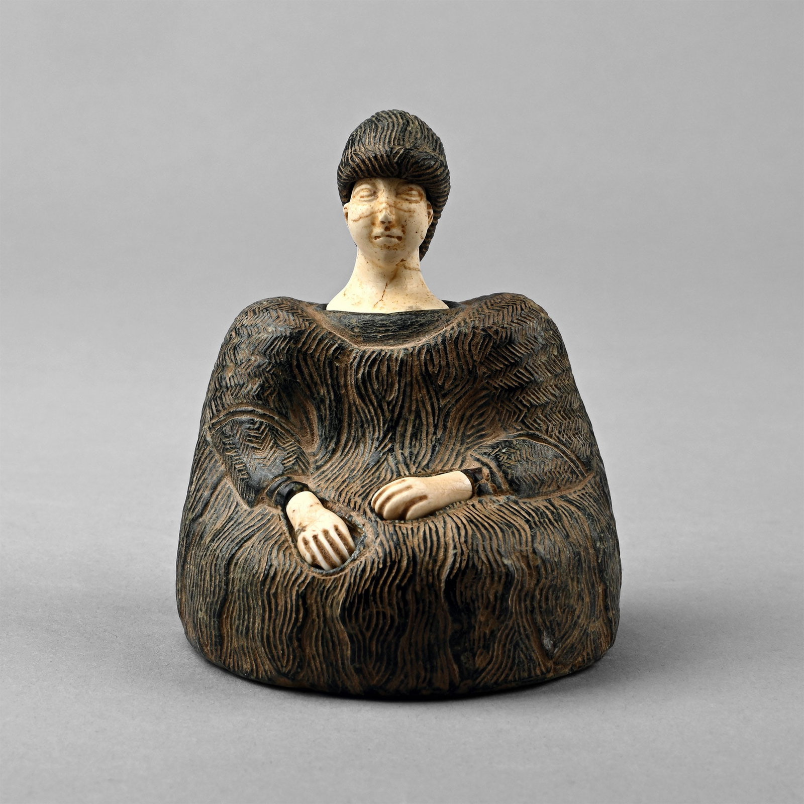 Bactrian Stone Female 'Princess' Idol: Bactria-Margiana, late 3rd-2nd millennium B.C. Carved as a seated human figure, body with rows of overlapping tufts of fur, set with a bald head carved from cream stone with semi-naturalistic detailin