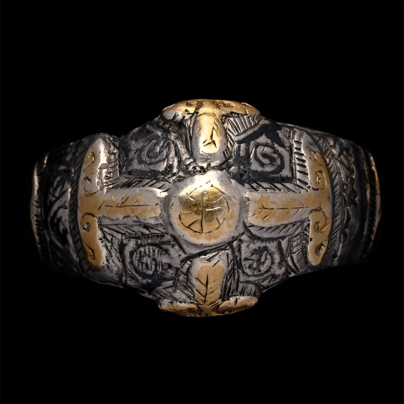 Seljuk Silver Ring with Gilt Cross: 11th-12th century A.D. Comprising a D-section hoop with expanding shoulders, a gilt shield with scrolls on each shoulder, and a low-relief cross expanding across the bezel with scrollwork background. 